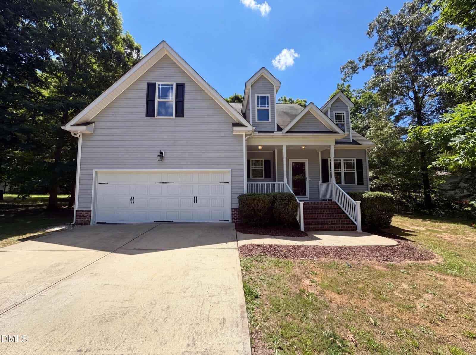 A two-story suburban house at 130 Green Forest Drive, Franklinton, features light siding, two front-facing gables, a covered porch, white garage door, and concrete driveway, all surrounded by trees and grass under a sunny blue sky.