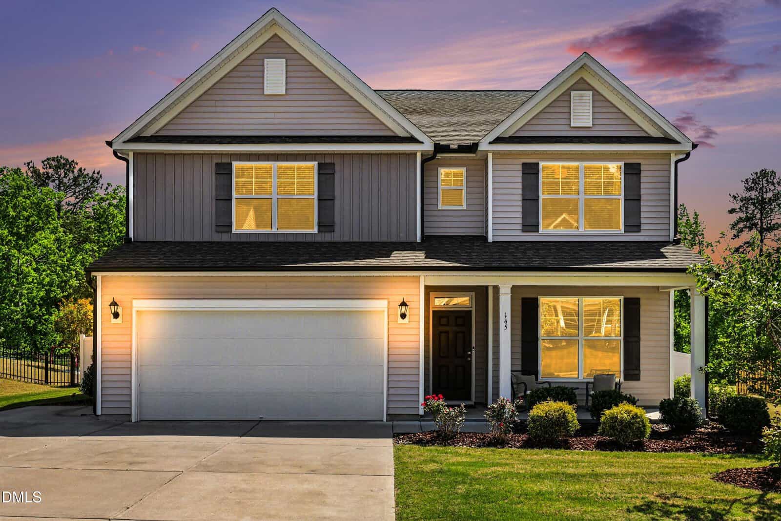 This two-story suburban house at 145 Kimberling Drive, Franklinton, features a double garage, gray siding with white trim, and warmly lit windows. A colorful sunset sky and neatly trimmed bushes complete the inviting front yard.