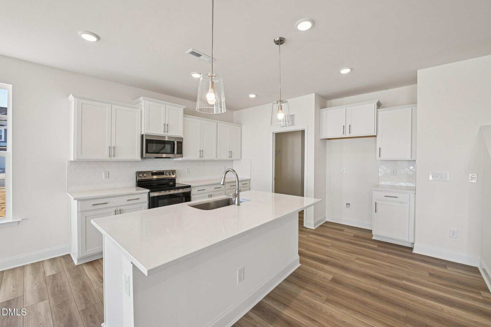 Bright modern kitchen at 109 Millview Way in Franklinton featuring white cabinets, stainless steel appliances, an island with a sink and pendant lights, and wood-look flooring. The space is clean, open, and minimalist in design.