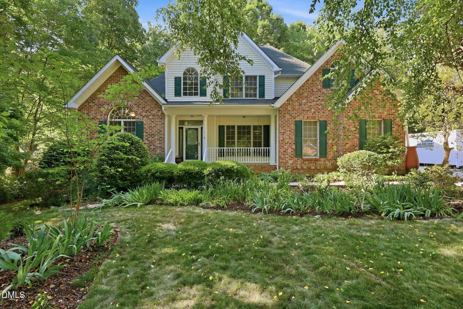 A two-story brick and siding house at 190 Georgetown Woods Drive in Youngsville, featuring green shutters, white trim, a covered front porch, and a landscaped front yard surrounded by trees and garden beds.