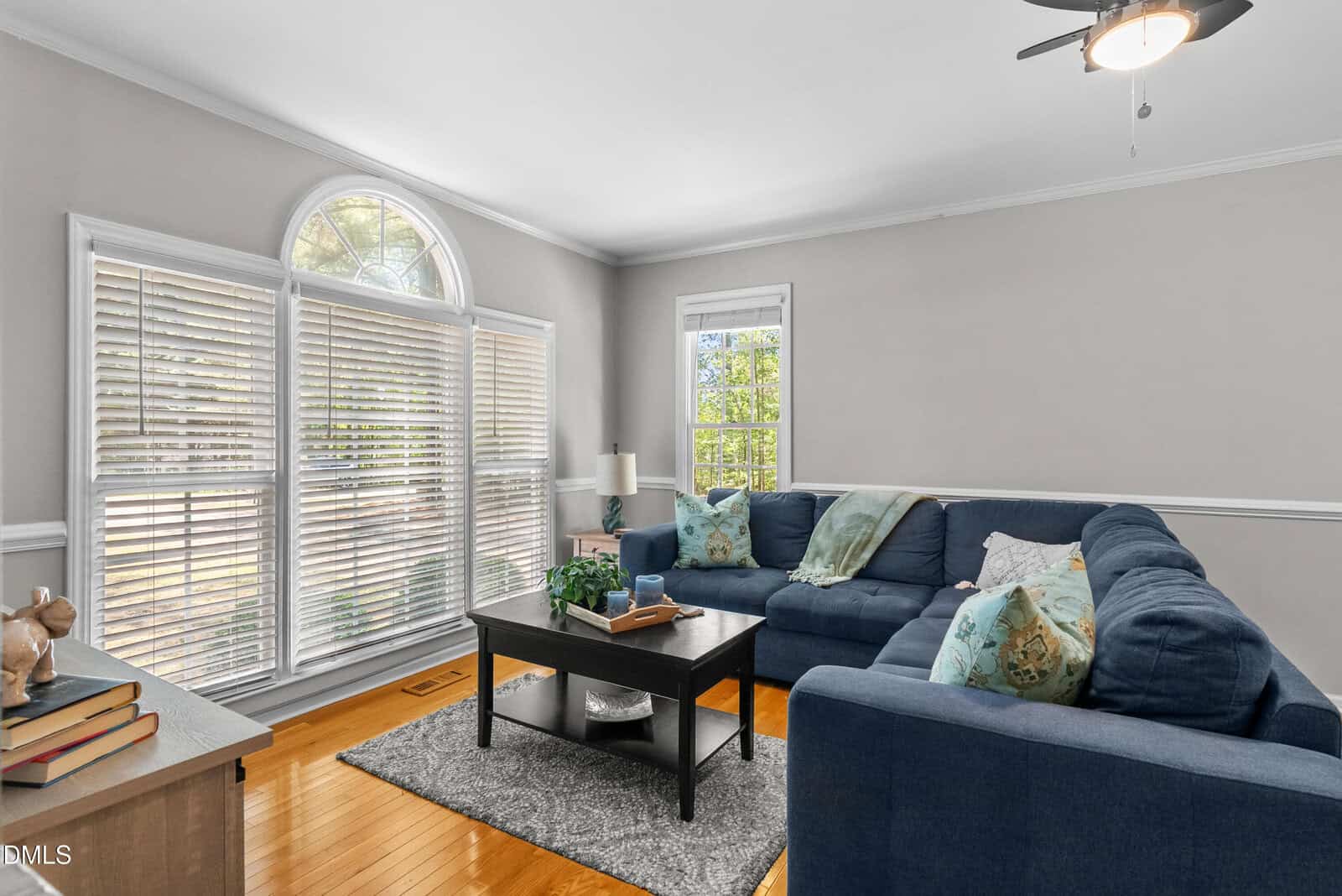 Bright living room with large arched window, blue sectional sofa, coffee table, and hardwood floors. Neutral walls and decor create a cozy, inviting atmosphere with plenty of natural light.