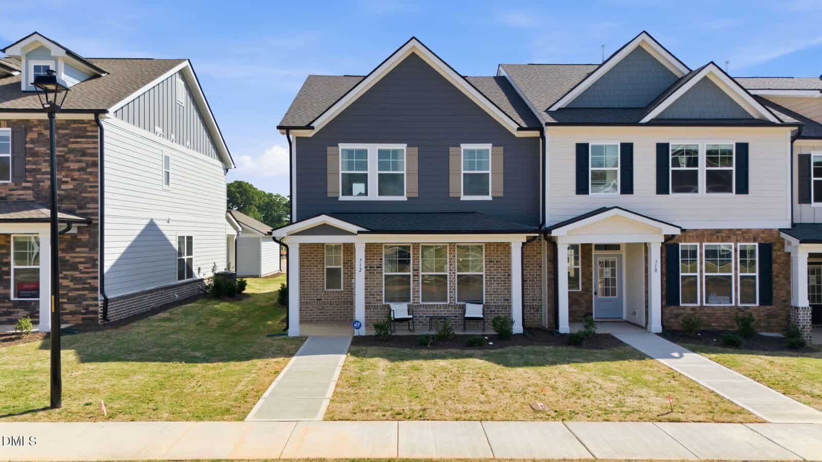 Two-story duplex at 712 Winton Way, Wake Forest, features brick and dark gray siding, white trim, and a covered porch. Sidewalk leads to the entrance with a small lawn and minimal landscaping under a clear blue sky.