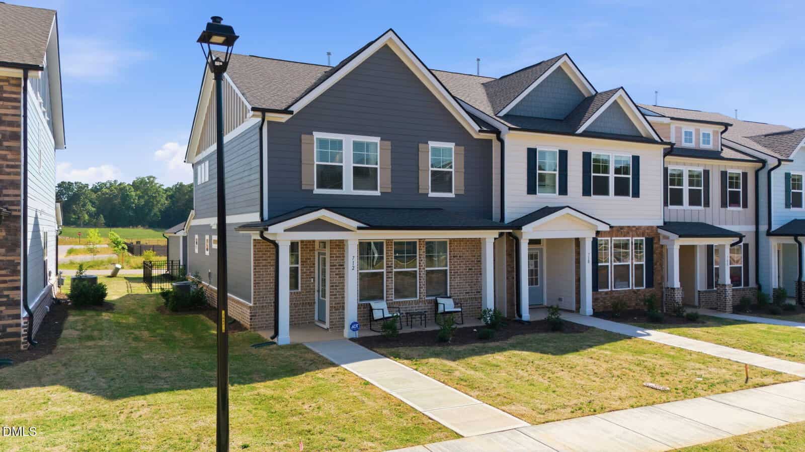 A row of modern, two-story townhouses with brick and siding exteriors, front porches, and neatly landscaped lawns under a clear blue sky.