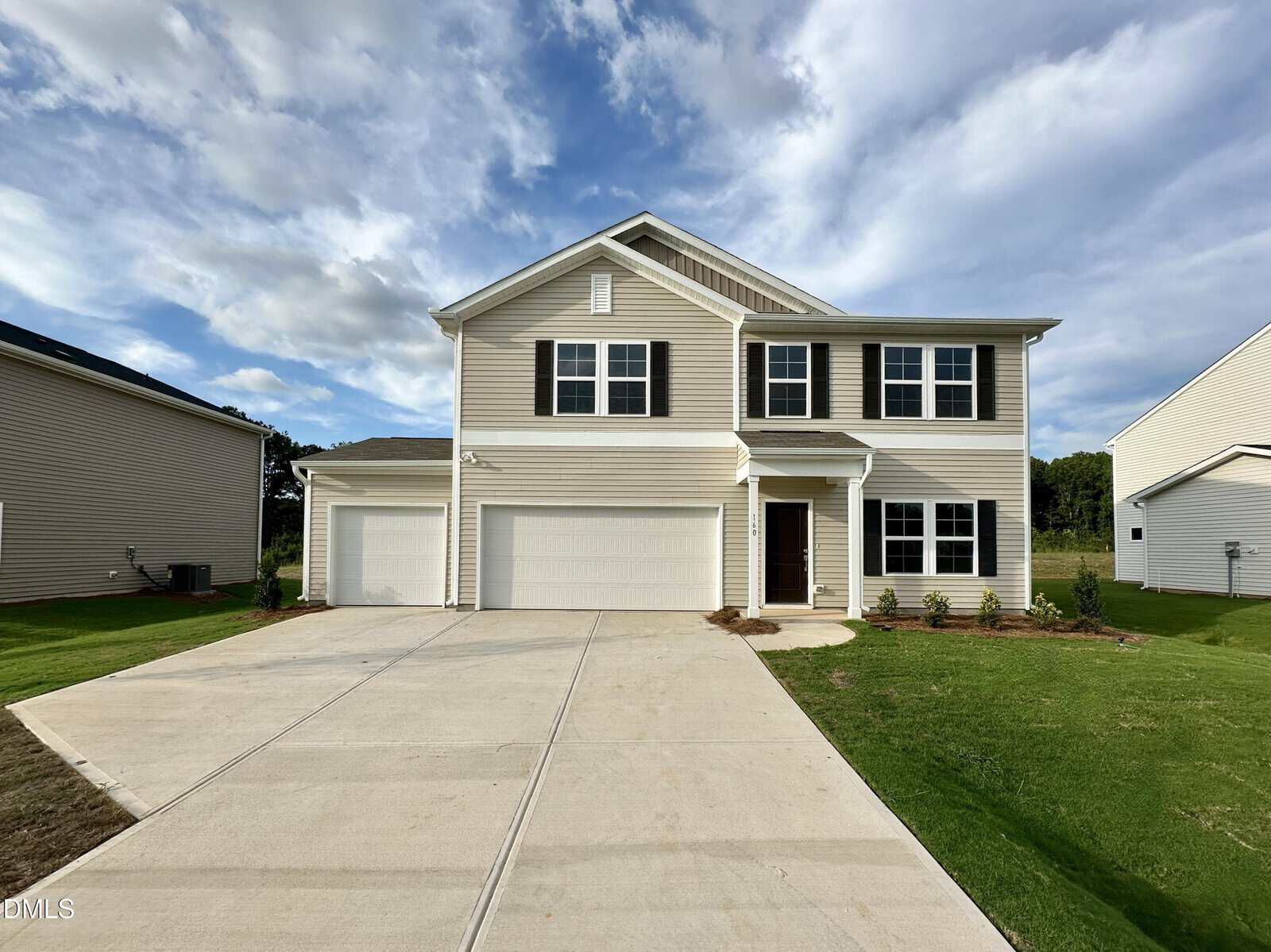 Two-story beige house with white trim, three-car garage, brown front door, and a wide driveway, set on a green lawn with some bushes under a partly cloudy blue sky—welcome to 160 Buckthorn Drive in Youngsville.