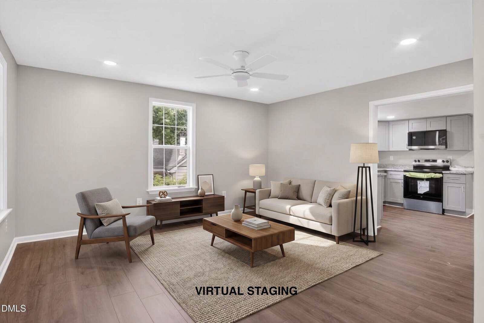A virtually staged living room at 904 Elm Street features a beige sofa, coffee table, armchair, TV stand, floor lamp, and rug on wood flooring. Light gray walls frame an open view into a kitchen with stainless steel appliances in Henderson.