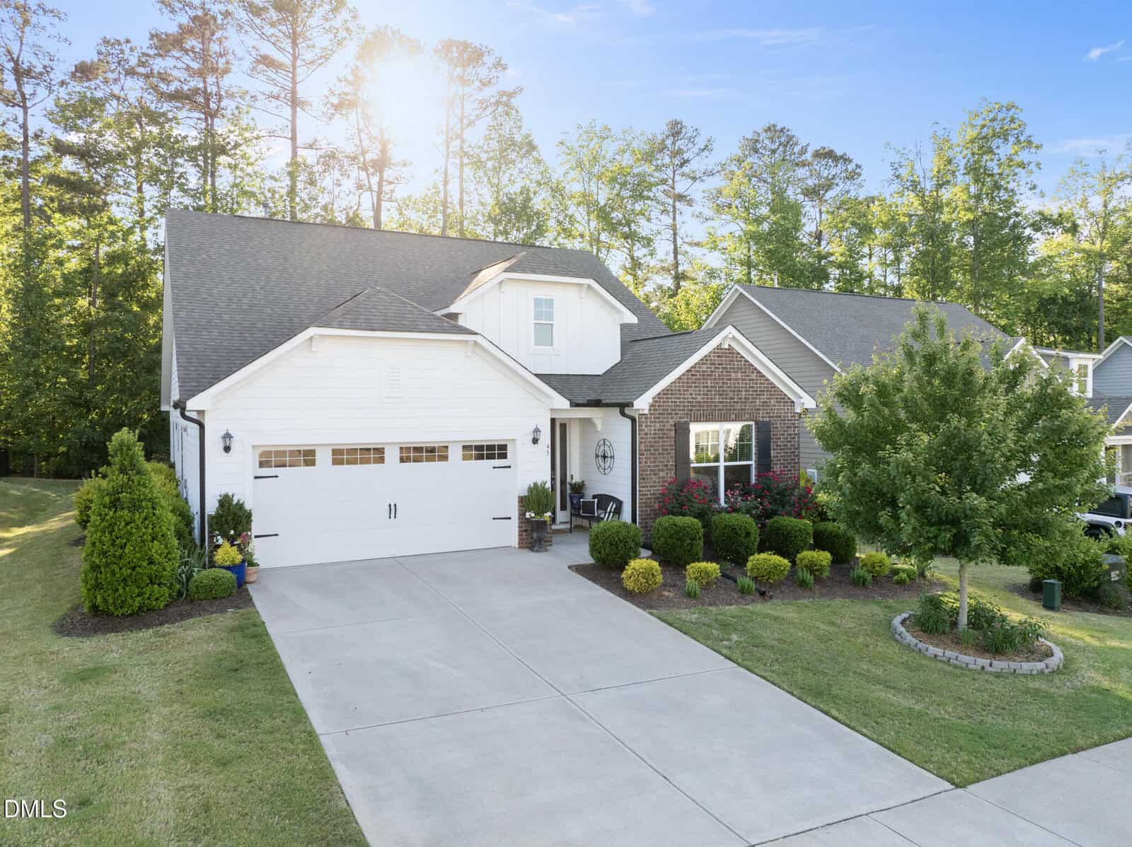 A modern suburban house at 45 Bramblewood Drive in Youngsville, featuring a two-car garage, white siding, and brick accents, is surrounded by neatly trimmed bushes, a green lawn, and trees in the background on a sunny day.
