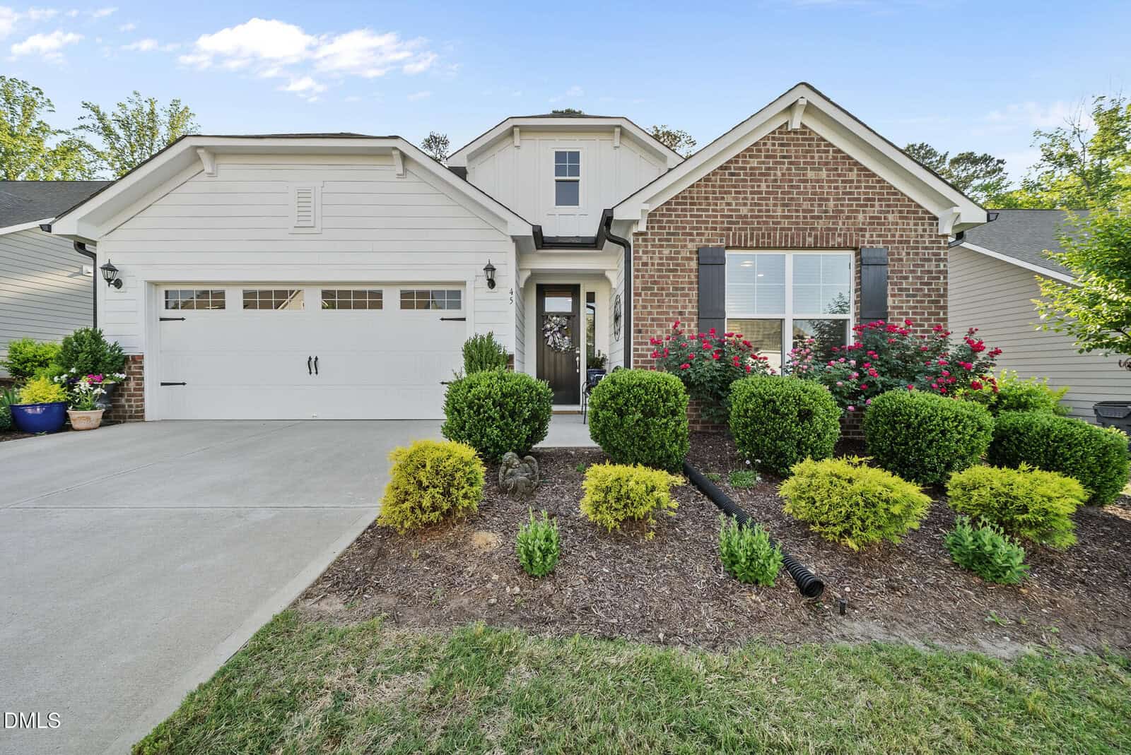 Charming single-story suburban home at 45 Bramblewood Drive, Youngsville, featuring a brick and white exterior, attached two-car garage, manicured bushes, flowering plants, and a concrete driveway leading to the entrance.