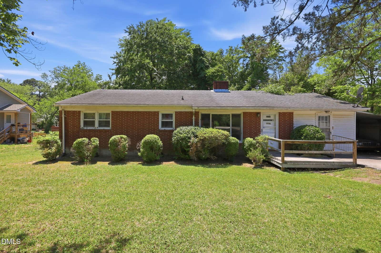 A single-story red brick house with white trim at 1315 Alpha Road in Henderson, featuring shrubs in front, a sloped roof, a carport and ramp on the right side, plus a grassy yard with trees and blue sky in the background.