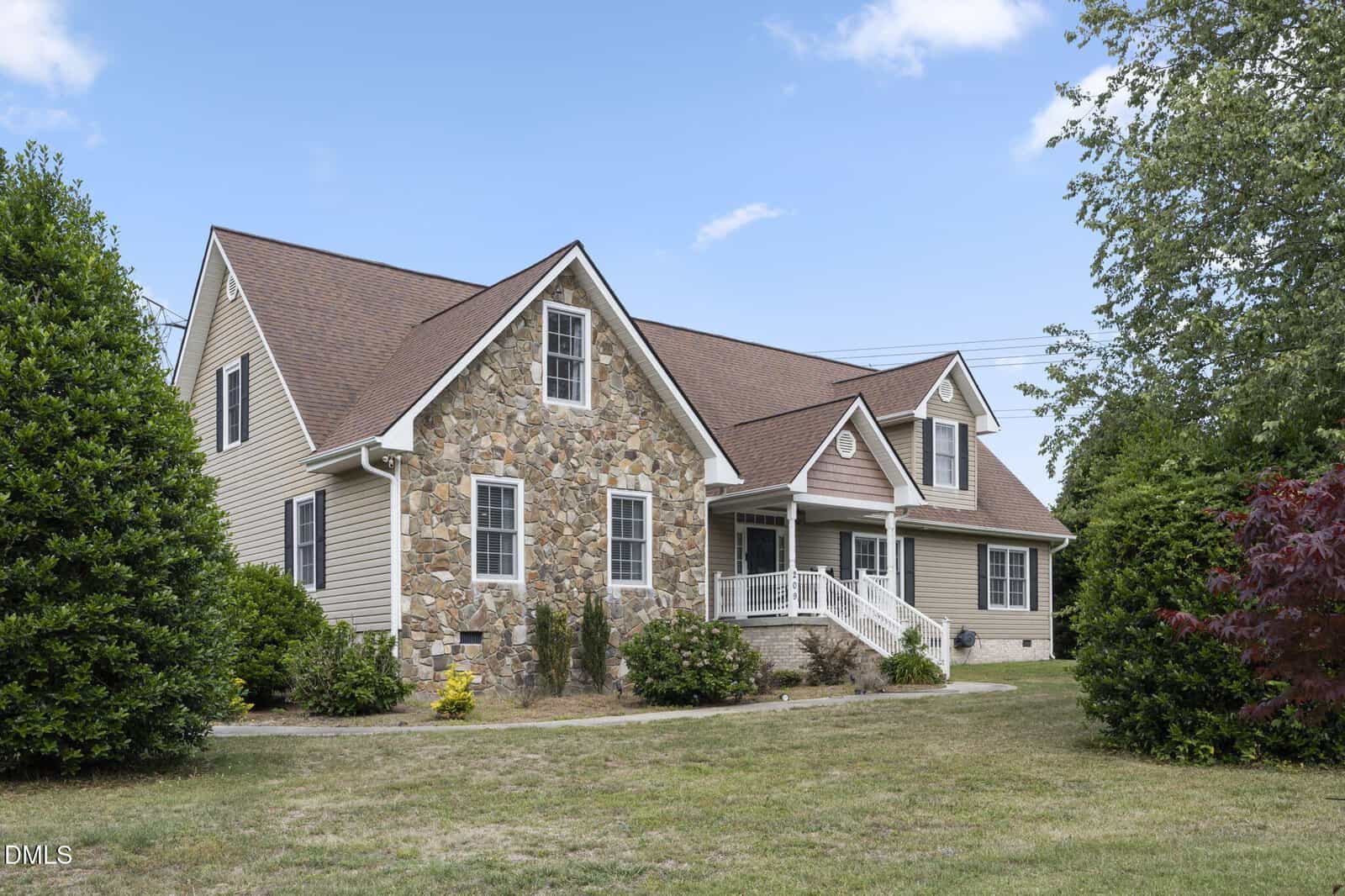 A two-story suburban house at 209 N Pointe Drive, Louisburg, features a stone and beige siding exterior, a covered front porch, and a gabled roof, surrounded by green shrubs and lawn under a blue sky with a few clouds.