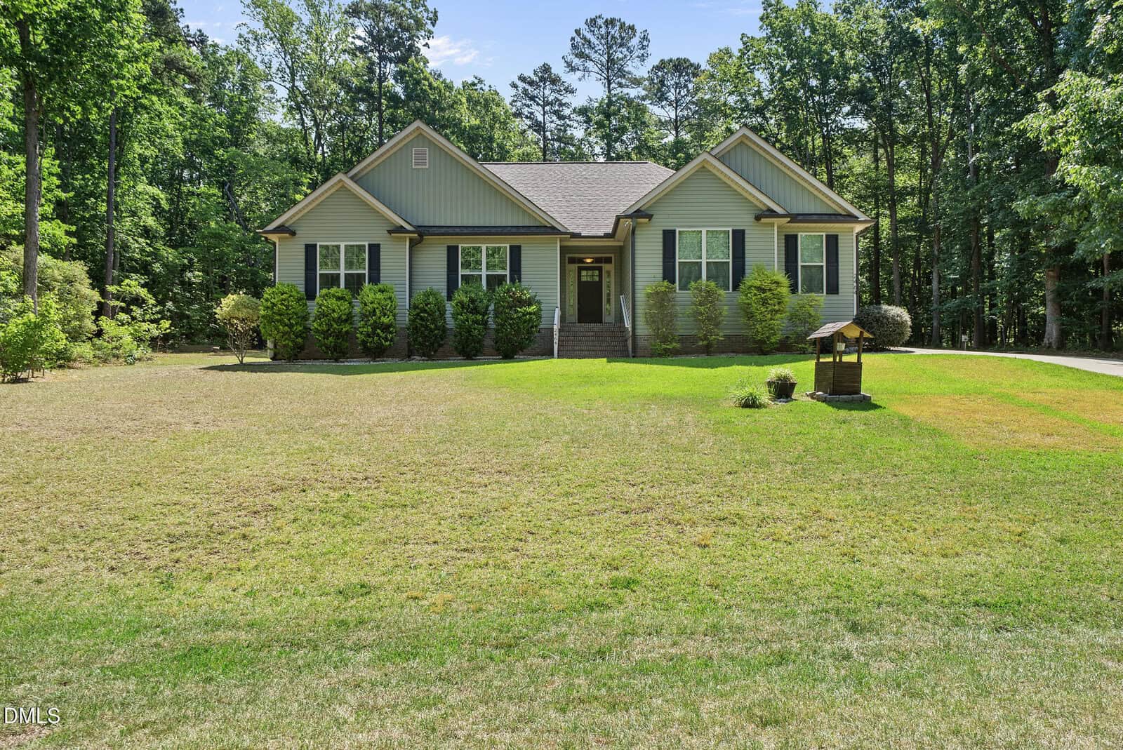 A single-story house with light green siding and white trim sits on a large, well-maintained lawn at 2464 Golden Forest Drive in Franklinton, with bushes by the entrance and trees surrounding the yard under a clear sky.