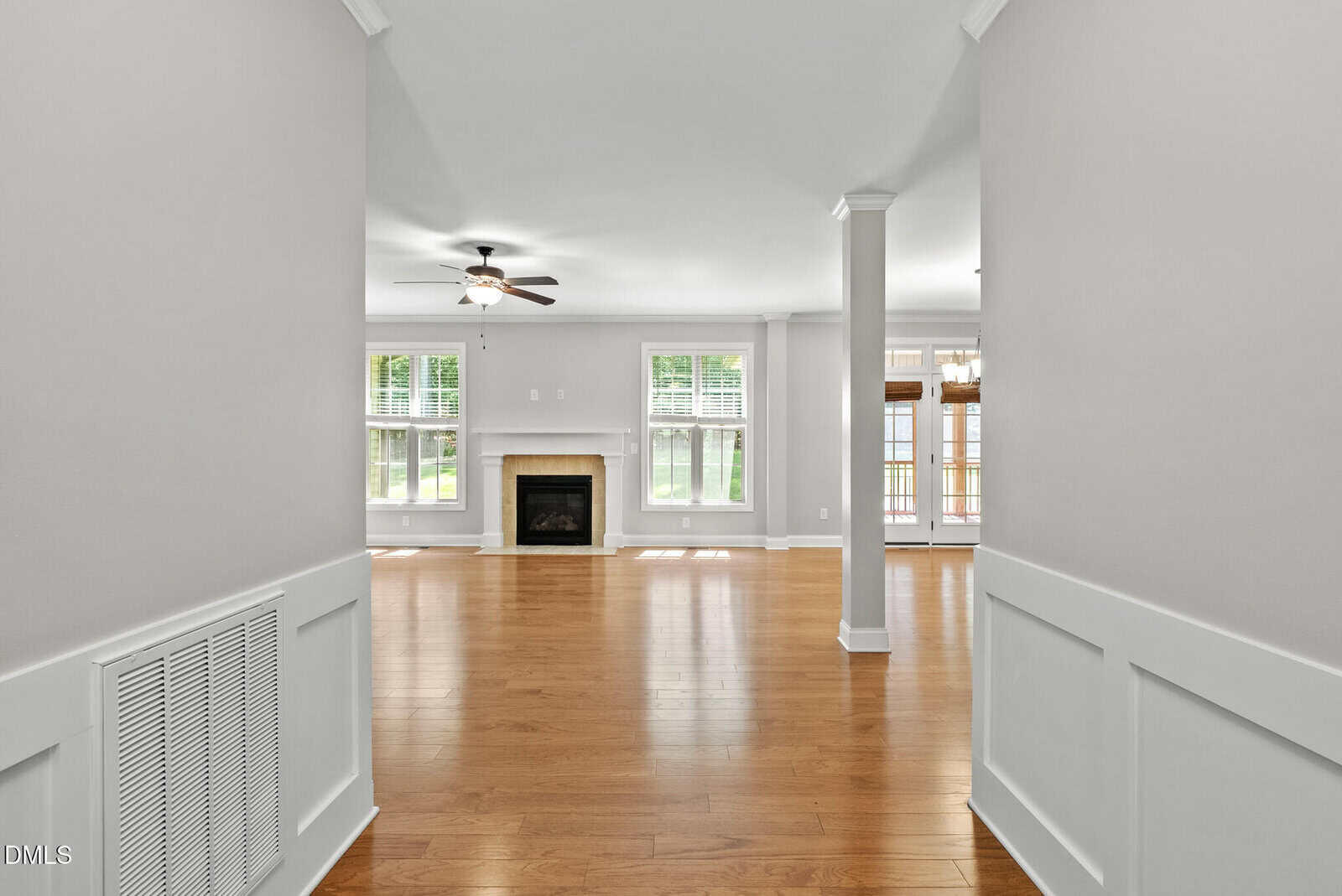 Bright, open living room with wood floors, white walls, a ceiling fan, a fireplace centered between two windows, and a connected dining area with large windows and a door leading outside.