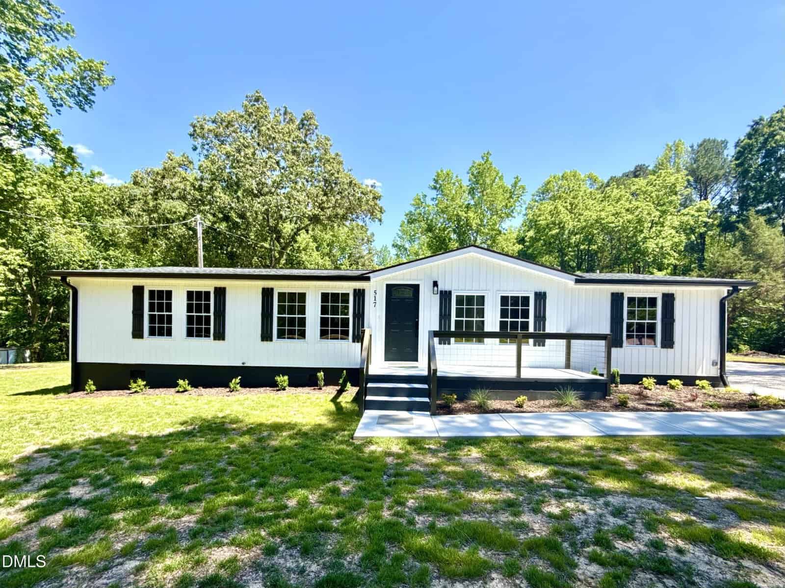 A white single-story house with black trim, wide front steps, and a ramp sits at 517 Sulphur Springs Road in Warrenton. The house is surrounded by a grassy yard and trees under a clear blue sky.