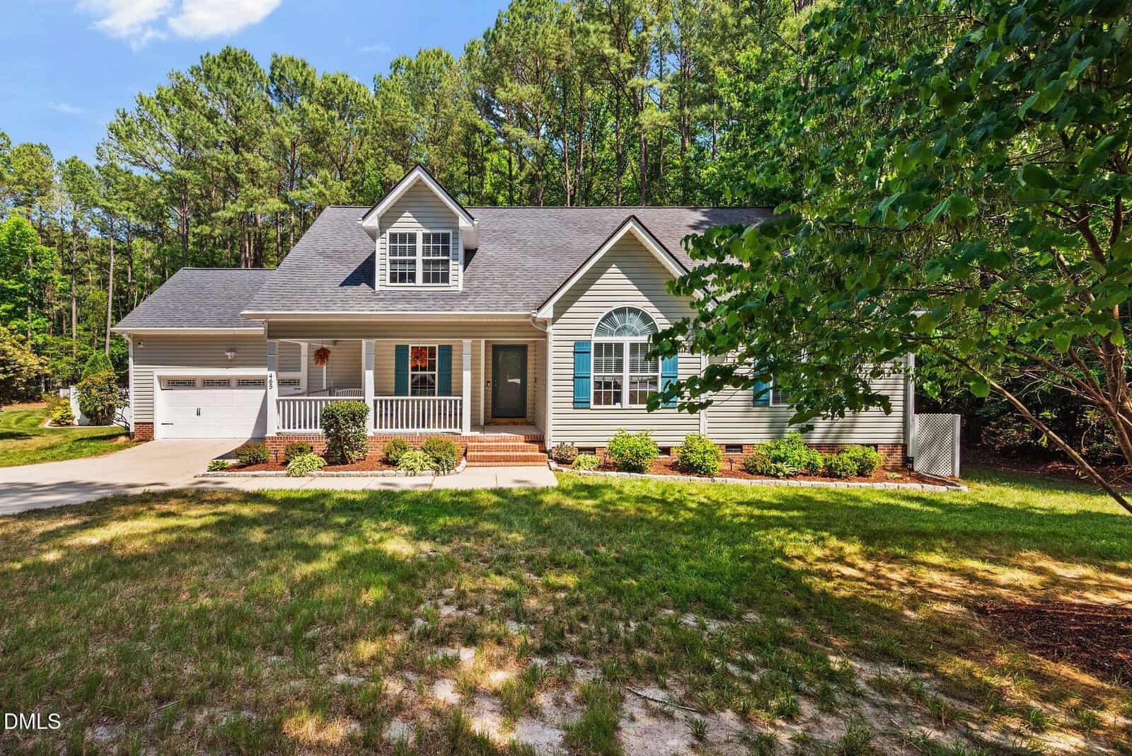 Charming single-story suburban house at 465 Spencer Gate Drive in Youngsville, featuring a gray exterior, white trim, front porch, attached garage, and a well-kept lawn bordered by tall trees under a blue sky.