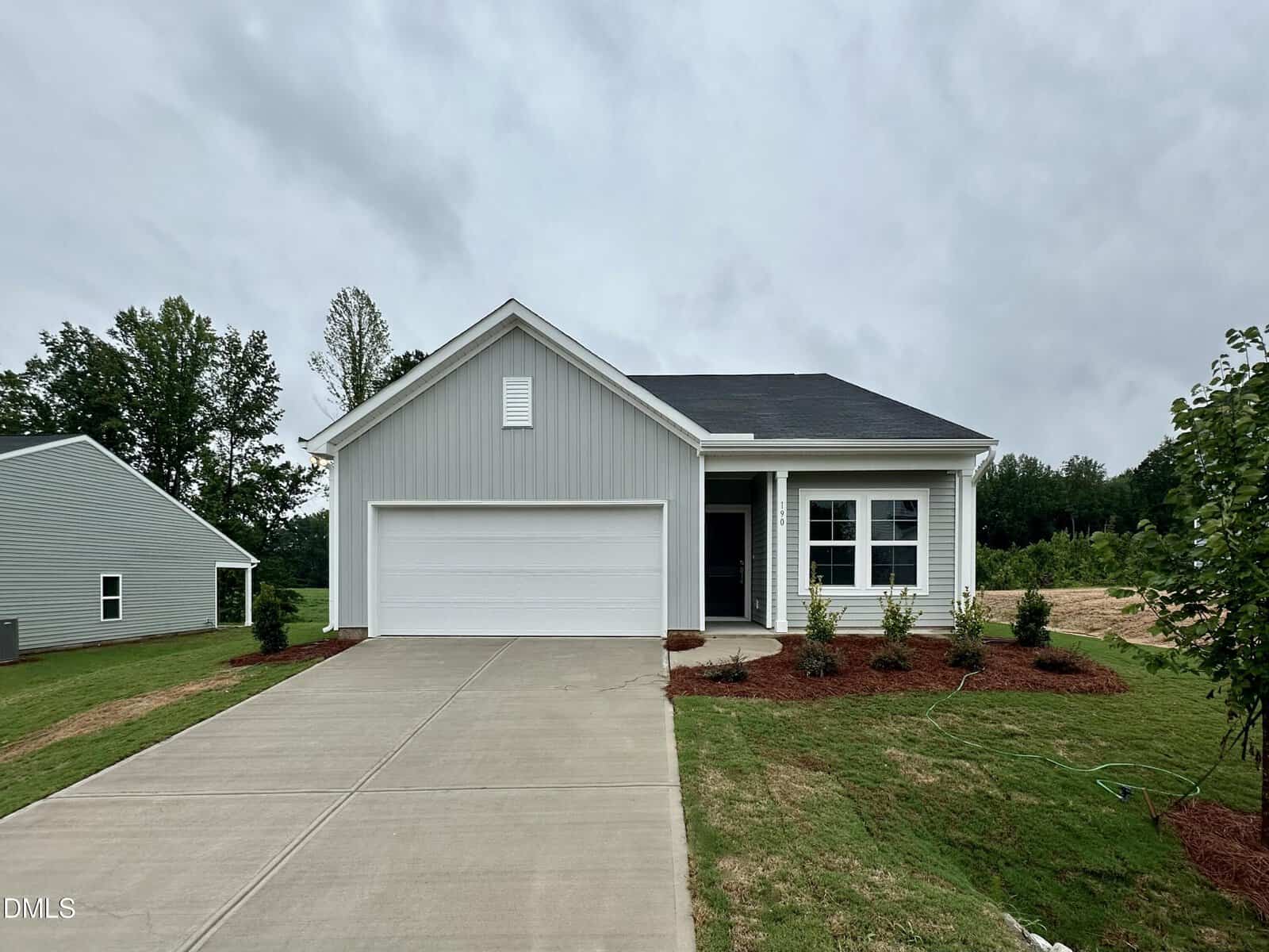 Single-story gray house at 190 Buckthorn Drive, Youngsville, with attached two-car garage, white trim, covered front porch, and landscaped yard with shrubs. Concrete driveway leads to the house; grass and trees are visible on either side under a cloudy sky.