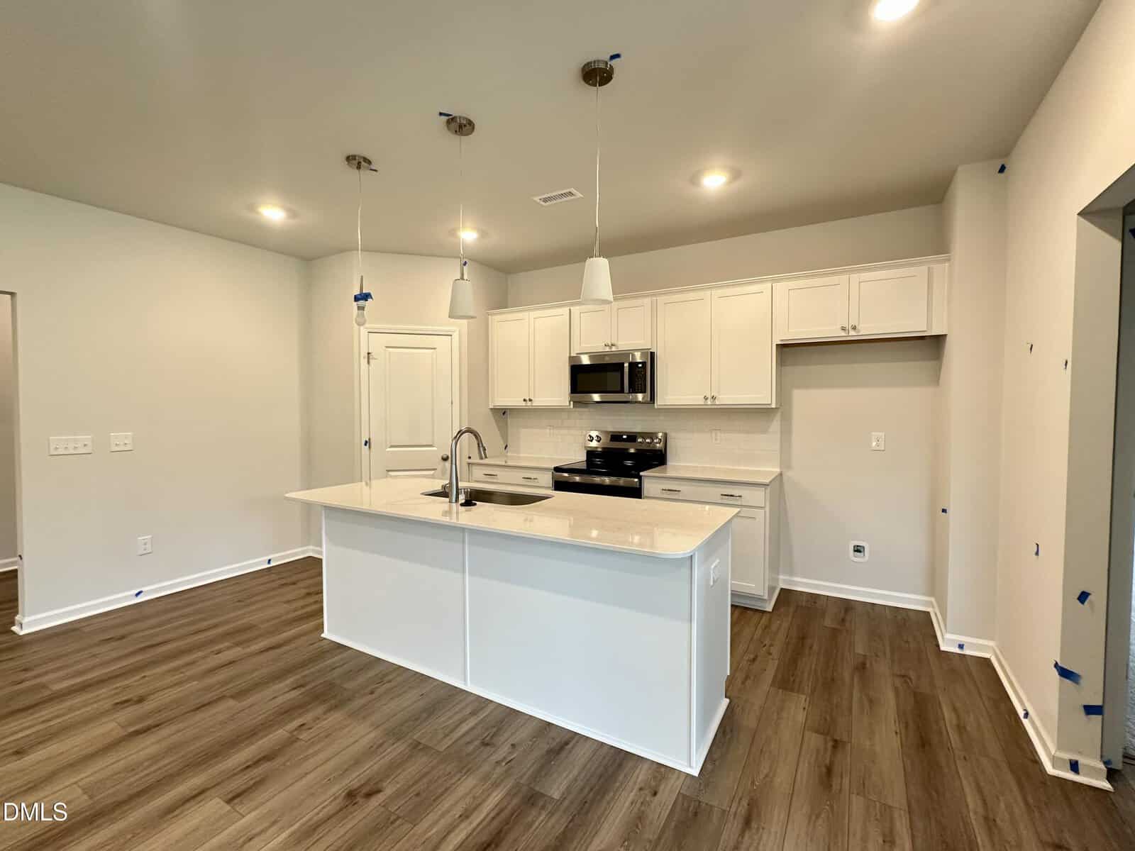 Modern kitchen with white cabinets, stainless steel appliances, an island with a sink, pendant lights, and wood-look flooring; walls are light-colored with recessed and pendant lighting.