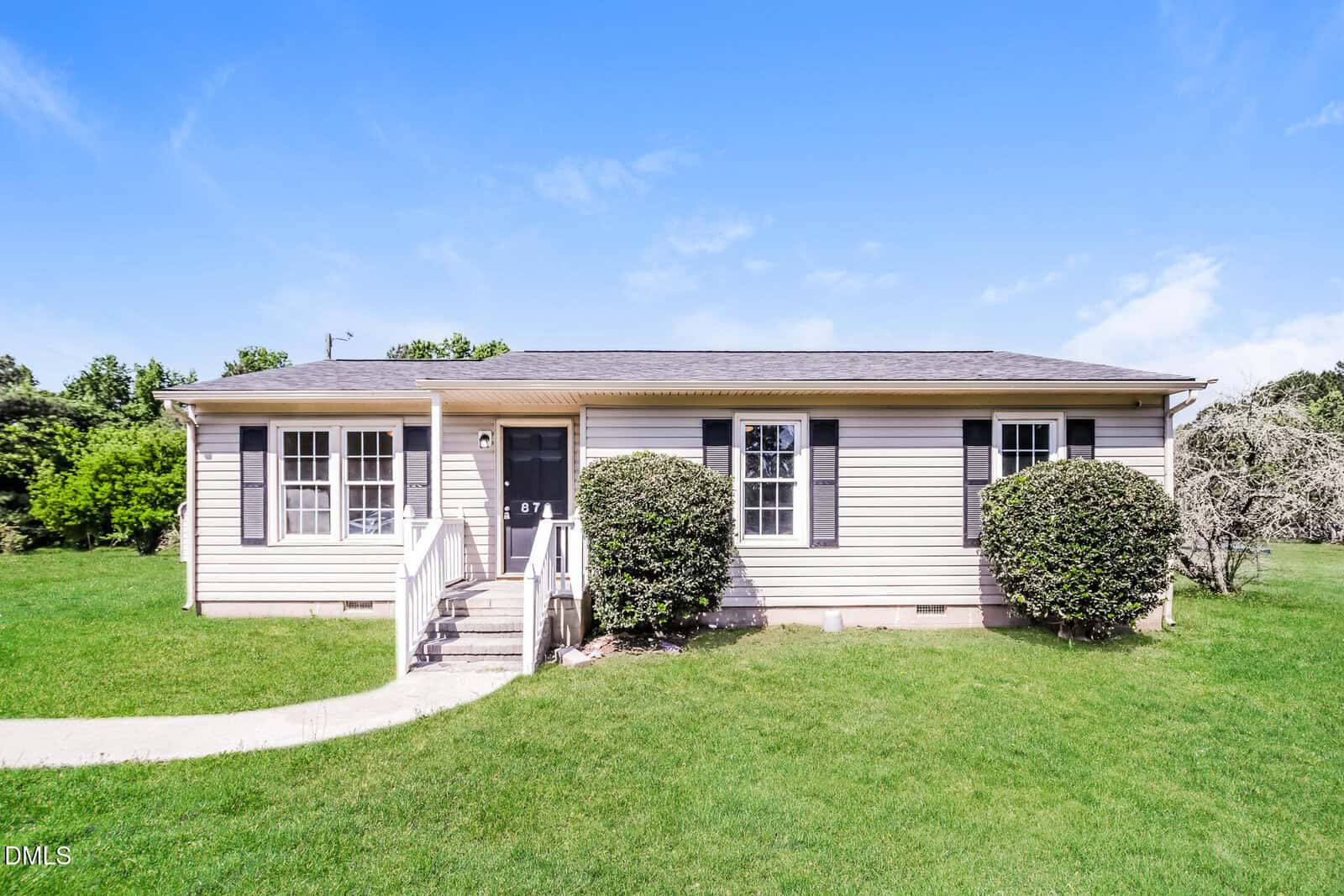 Charming single-story beige house at 870 Abbott Road in Henderson with black shutters, central front door, small porch with white railings, surrounded by green lawn and bushes, under a clear blue sky.