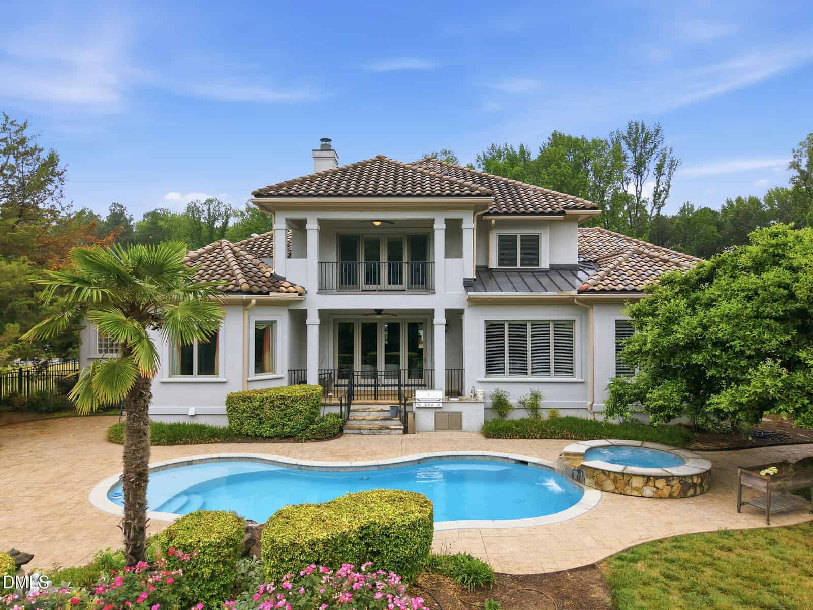 Located at 305 Hidden Lake Drive in Youngsville, this large two-story white house with a tiled roof features a balcony, numerous windows, a landscaped yard, an in-ground pool, hot tub, and surrounding trees under a clear blue sky.