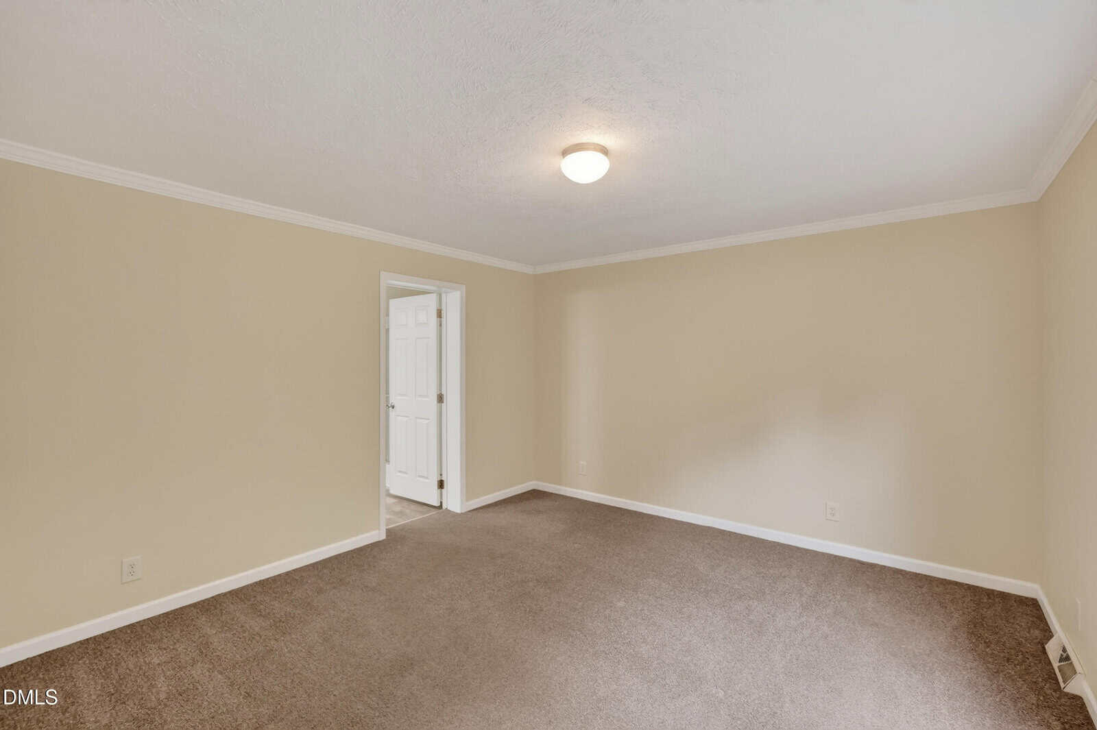 Empty room with beige walls, white trim, brown carpet, a ceiling light, and an open doorway leading to another room with a white door.