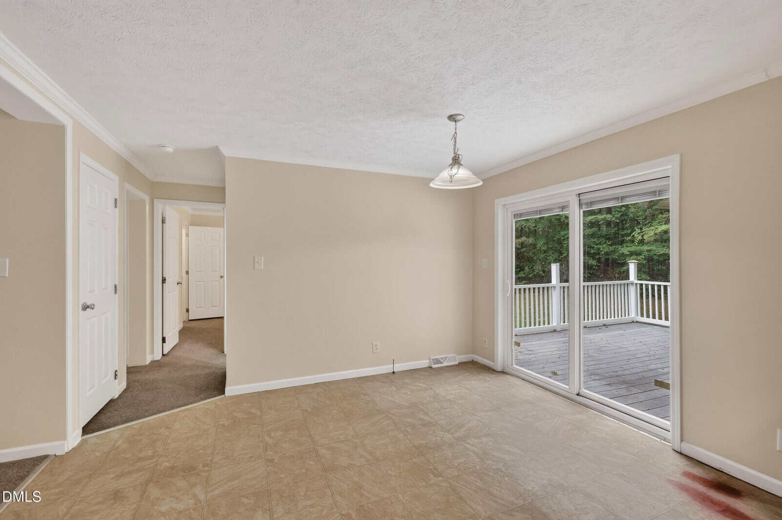 A beige-walled room with a hanging light fixture, tile flooring, sliding glass doors leading to a deck, and a hallway with doorways to other rooms.