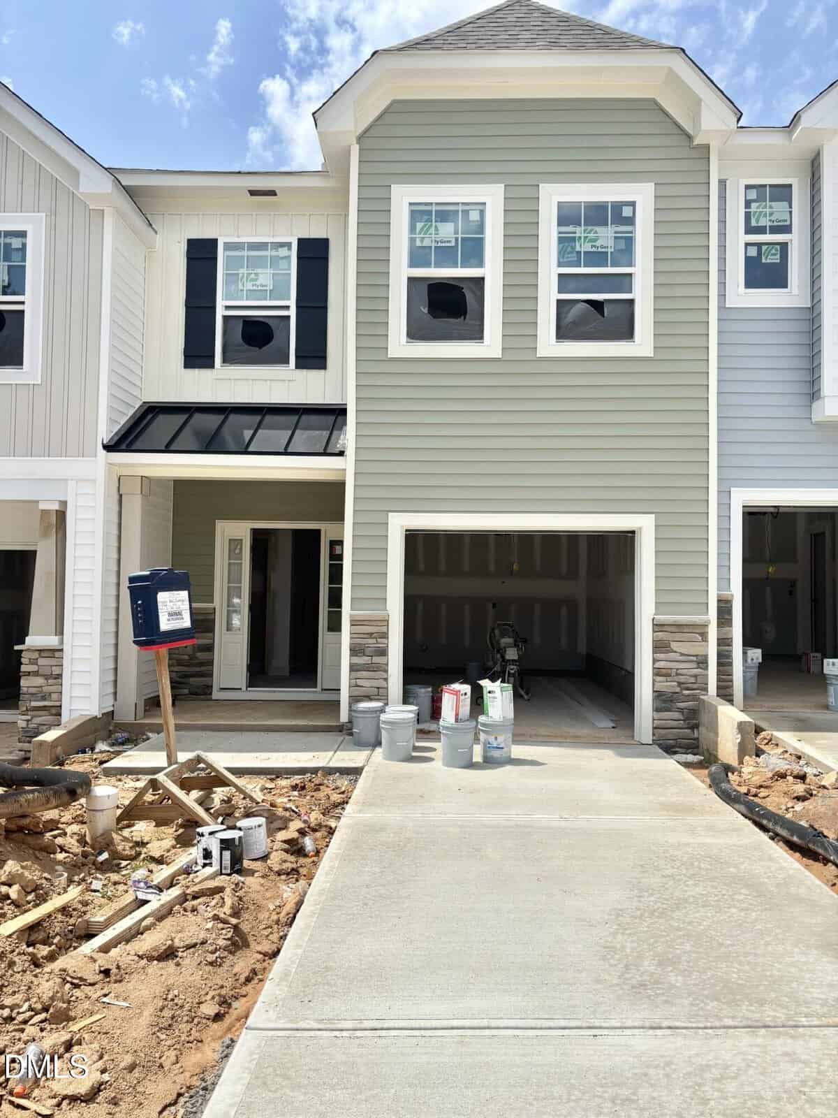 Newly constructed townhouse in Franklinton at 202 Carnaby Lane 132, featuring light green siding, stone accents, a single garage, and a covered entryway. Construction materials and supplies are visible on the driveway and yard.