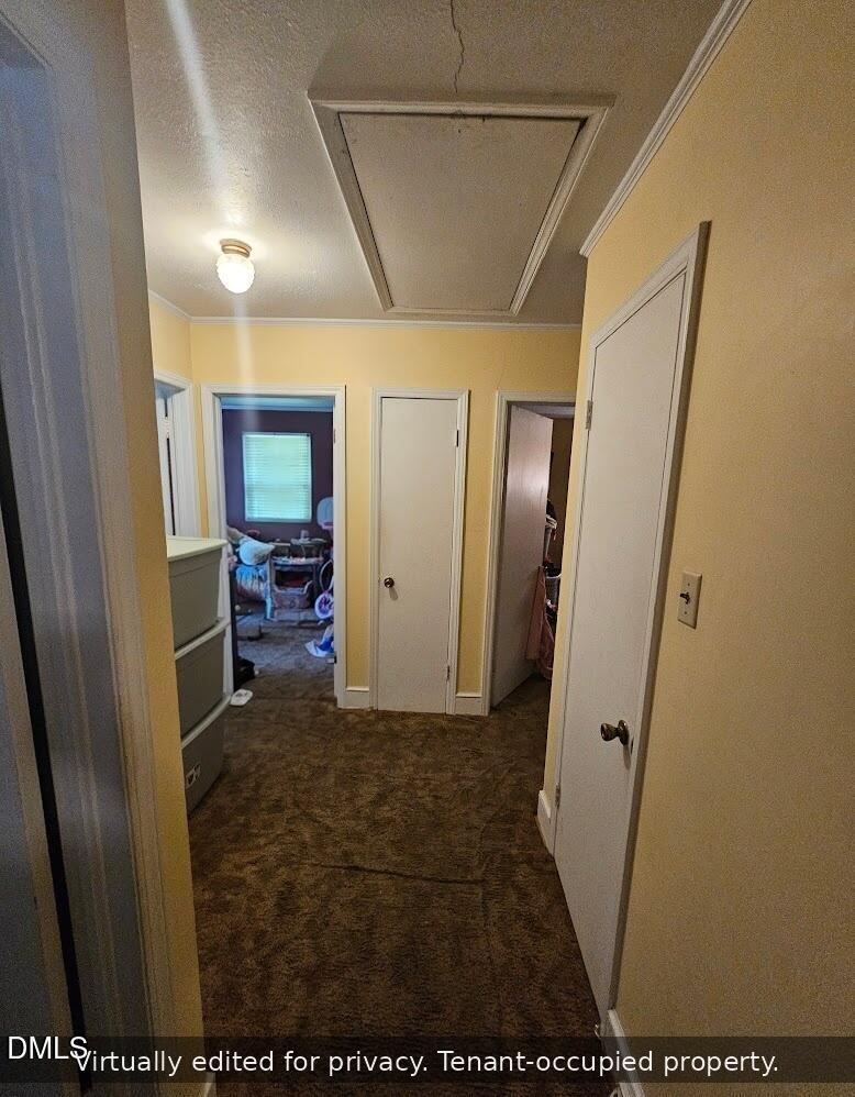 A narrow hallway with yellow walls and brown carpet, featuring three closed white doors. A lit ceiling light and an attic hatch are visible. A cluttered room with toys can be seen through the open doorway at the end.