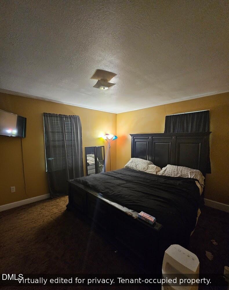 A bedroom with mustard-yellow walls, a black bedframe and bedding, a standing lamp with colorful shades, a wall-mounted TV, a mirror, and two windows with dark curtains. Text reads: “Virtually edited for privacy. Tenant-occupied property.”.