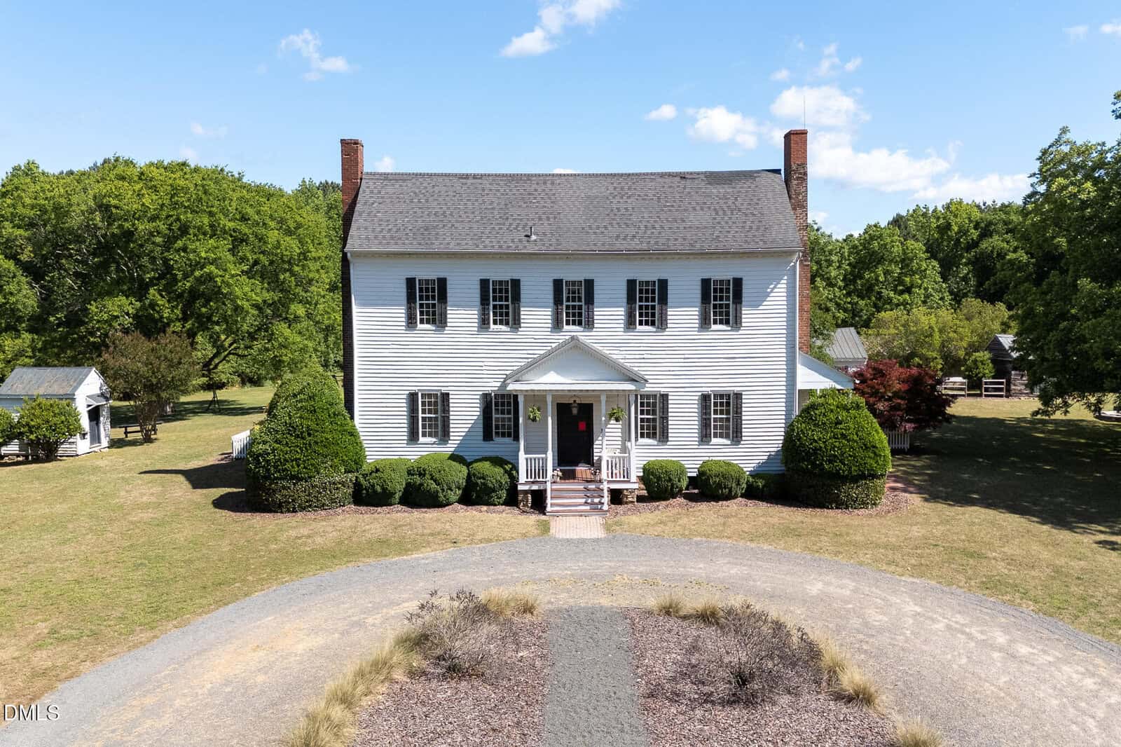 A large, white, two-story colonial-style house at 3679 Oak Lawn Farm Road, Oxford, features black shutters, brick chimneys, a covered front porch, and is surrounded by neatly trimmed bushes, trees, and a circular gravel driveway.