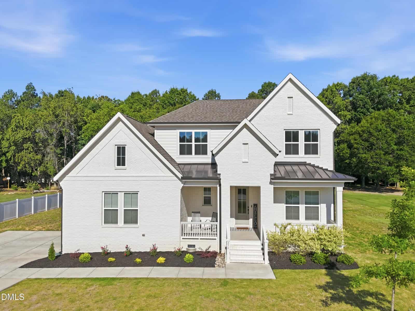 A modern two-story white house at 230 Scotland Drive, Youngsville, with a covered front porch, manicured landscaping, and a green lawn, set against a backdrop of trees and blue sky.