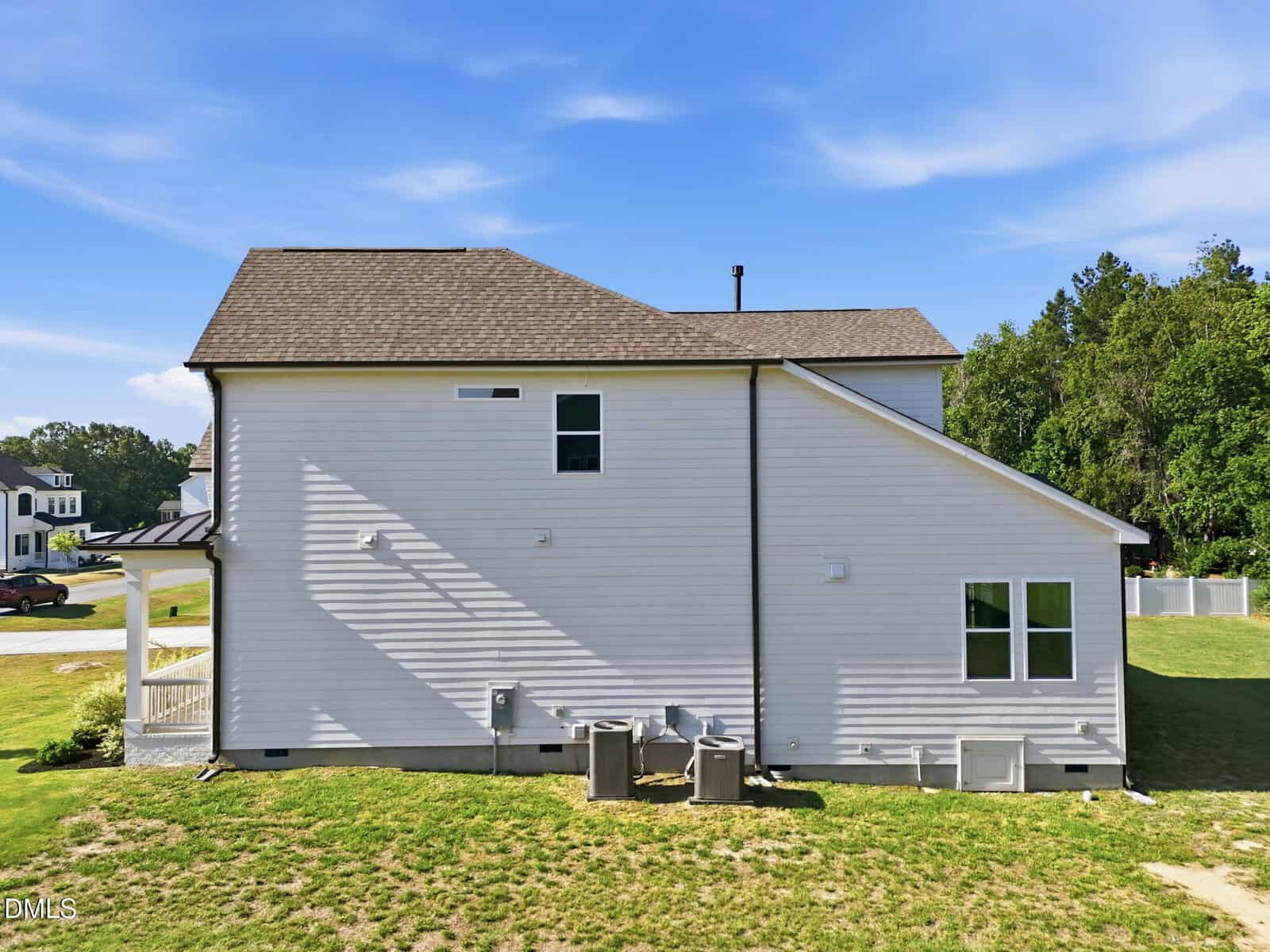 A modern two-story house with white siding, a brown shingle roof, and multiple rectangular windows, viewed from the side. The yard is grassy with some outdoor HVAC units and trees in the background.
