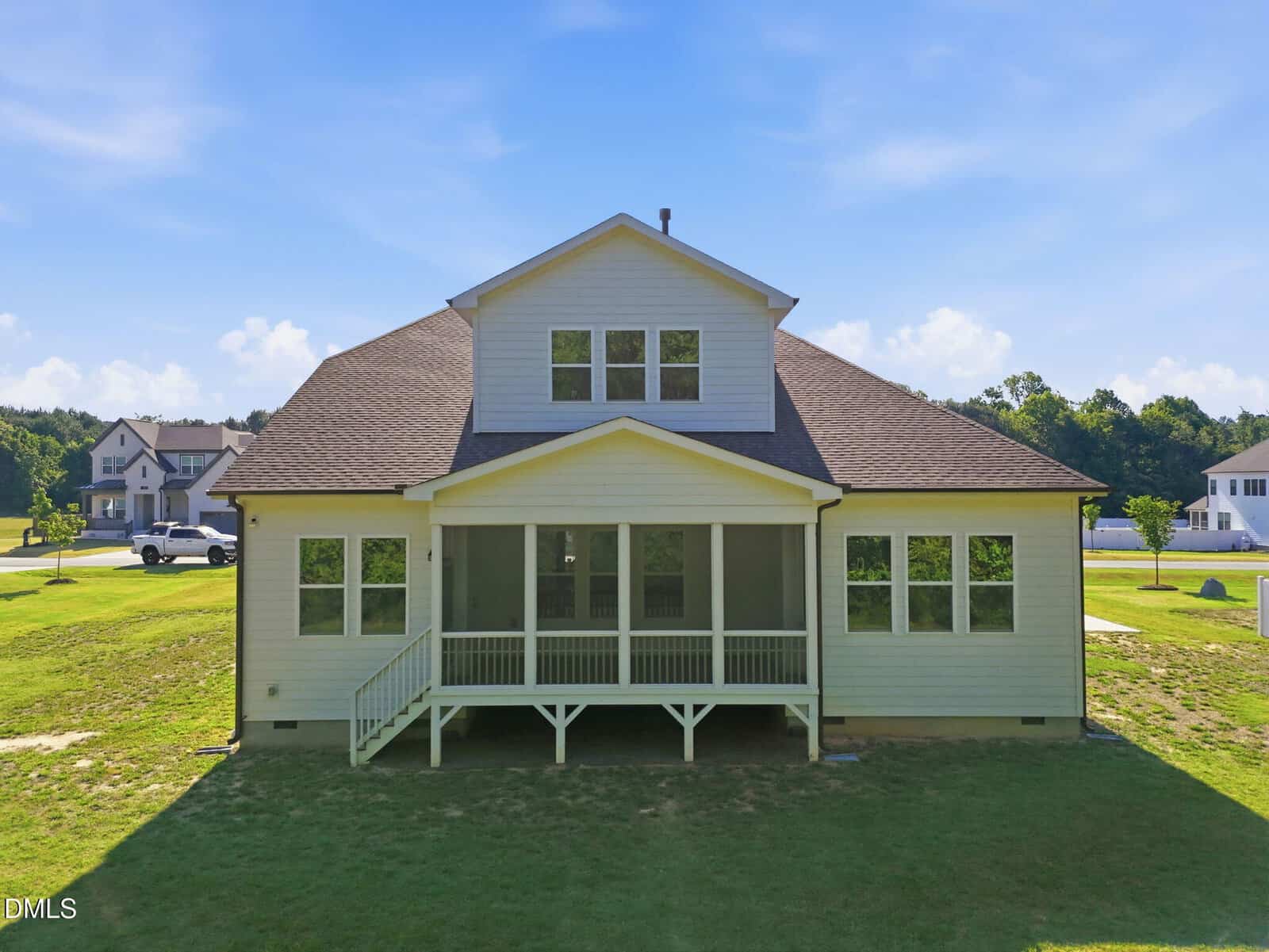 A two-story house with a covered back porch, surrounded by a grassy yard and neighboring homes under a blue sky with scattered clouds.