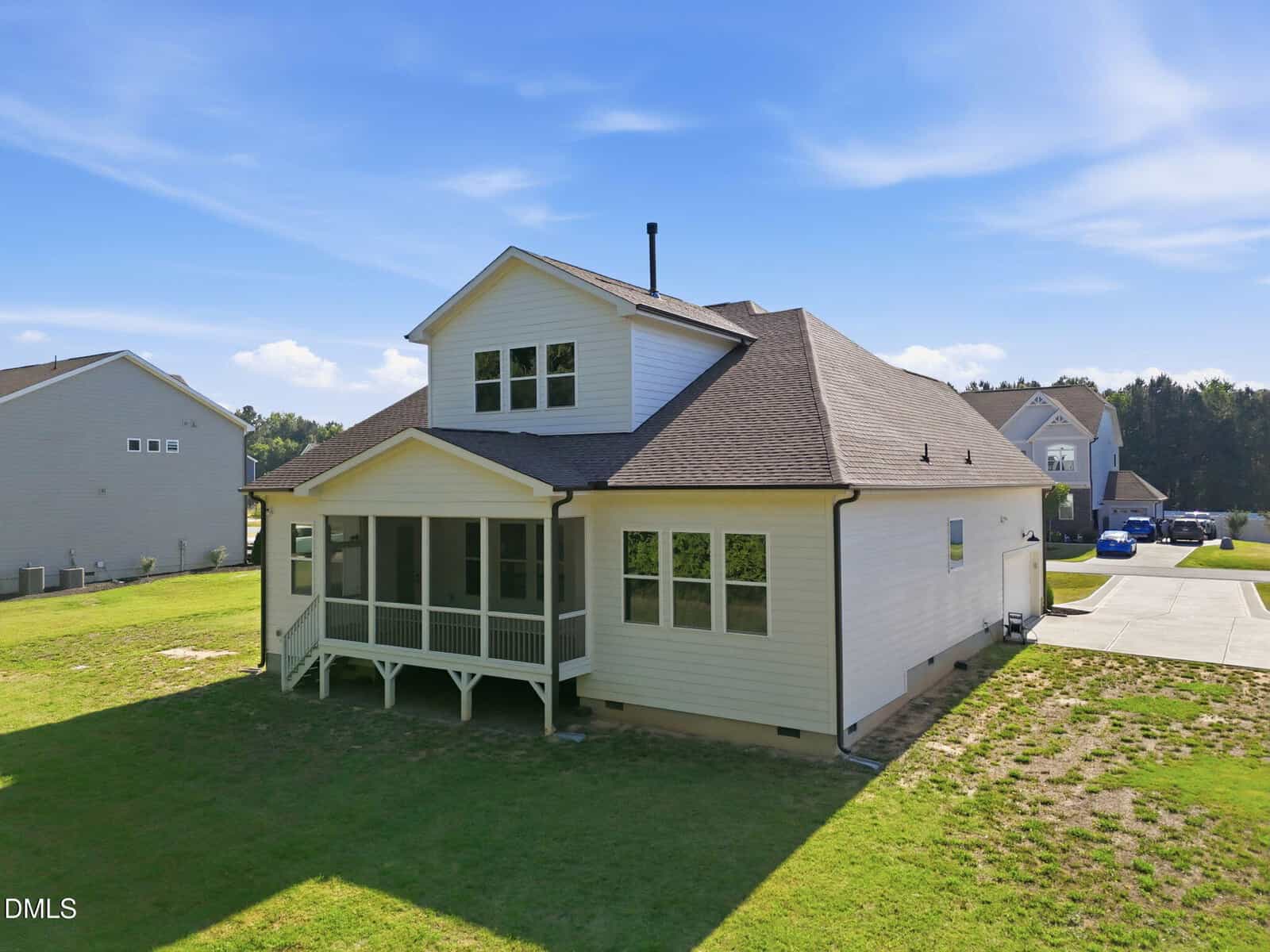 A two-story white house with a screened porch and large windows sits on a grassy yard under a blue sky, with neighboring homes and a driveway visible nearby.