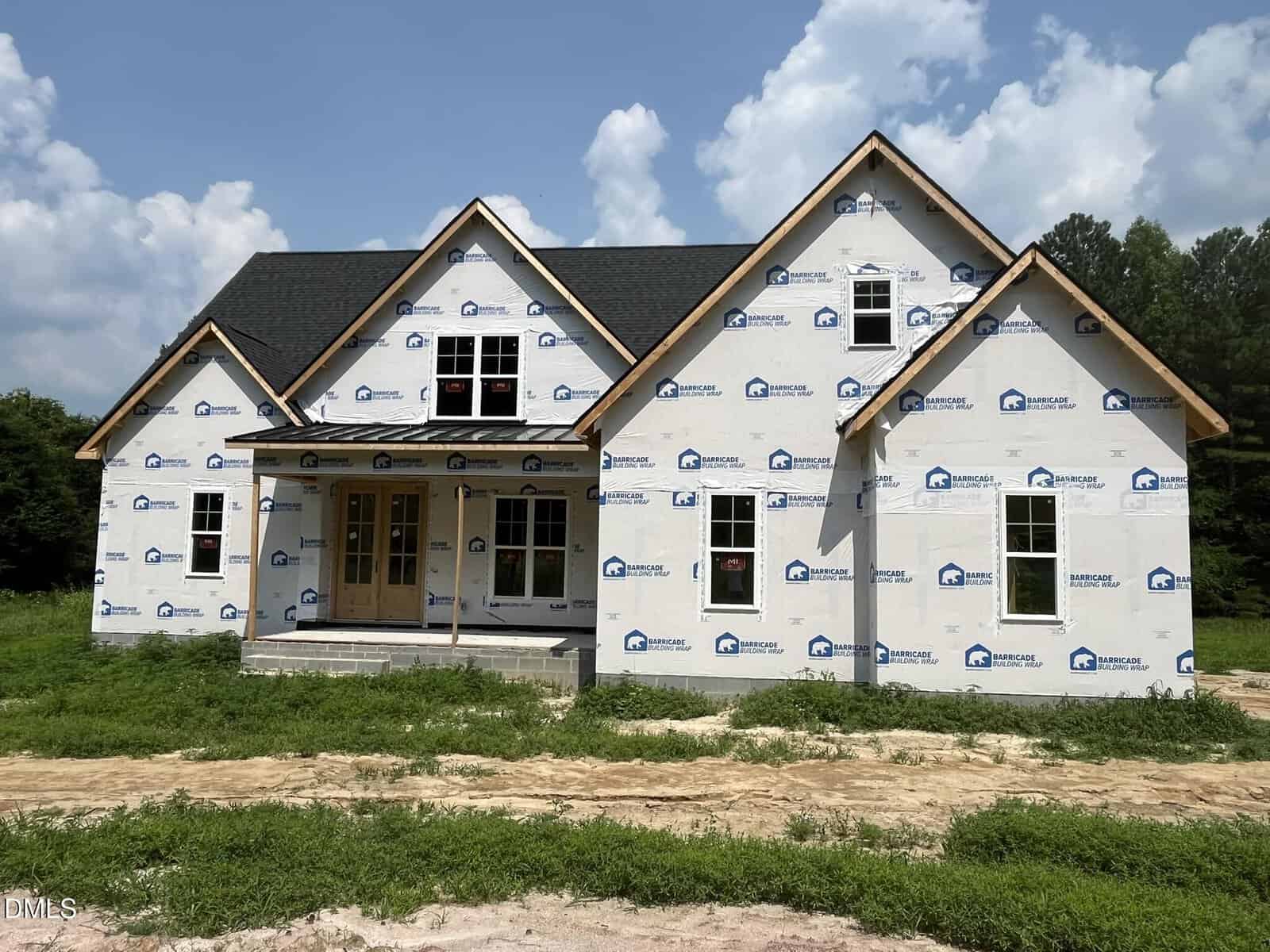 A partially constructed house with house wrap, black roof shingles, unfinished yard, and a covered front porch sits on Lot 4b Flat Rock Road in Franklinton, set against a partly cloudy sky and treeline in the background.