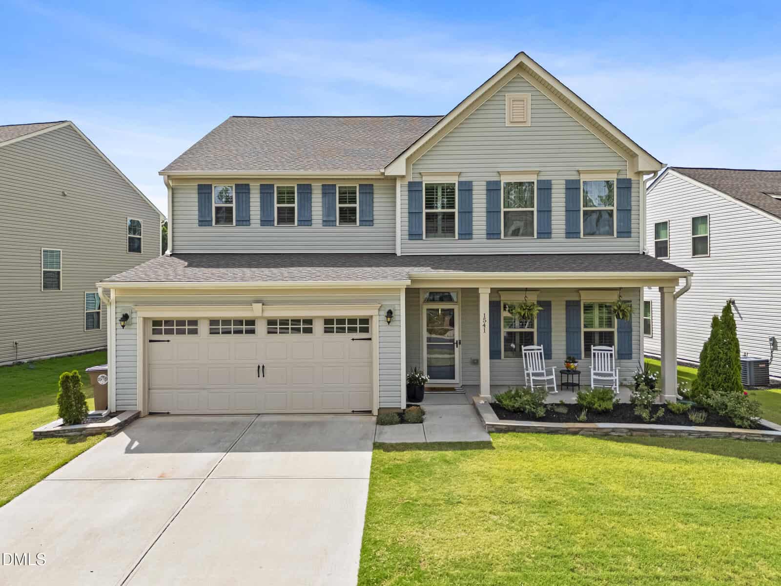 Charming two-story suburban house at 1541 Ripley Woods Street, Wake Forest. Light blue siding, white trim, blue shutters, double garage, front porch with rocking chairs, manicured lawn, and neatly landscaped garden beds.