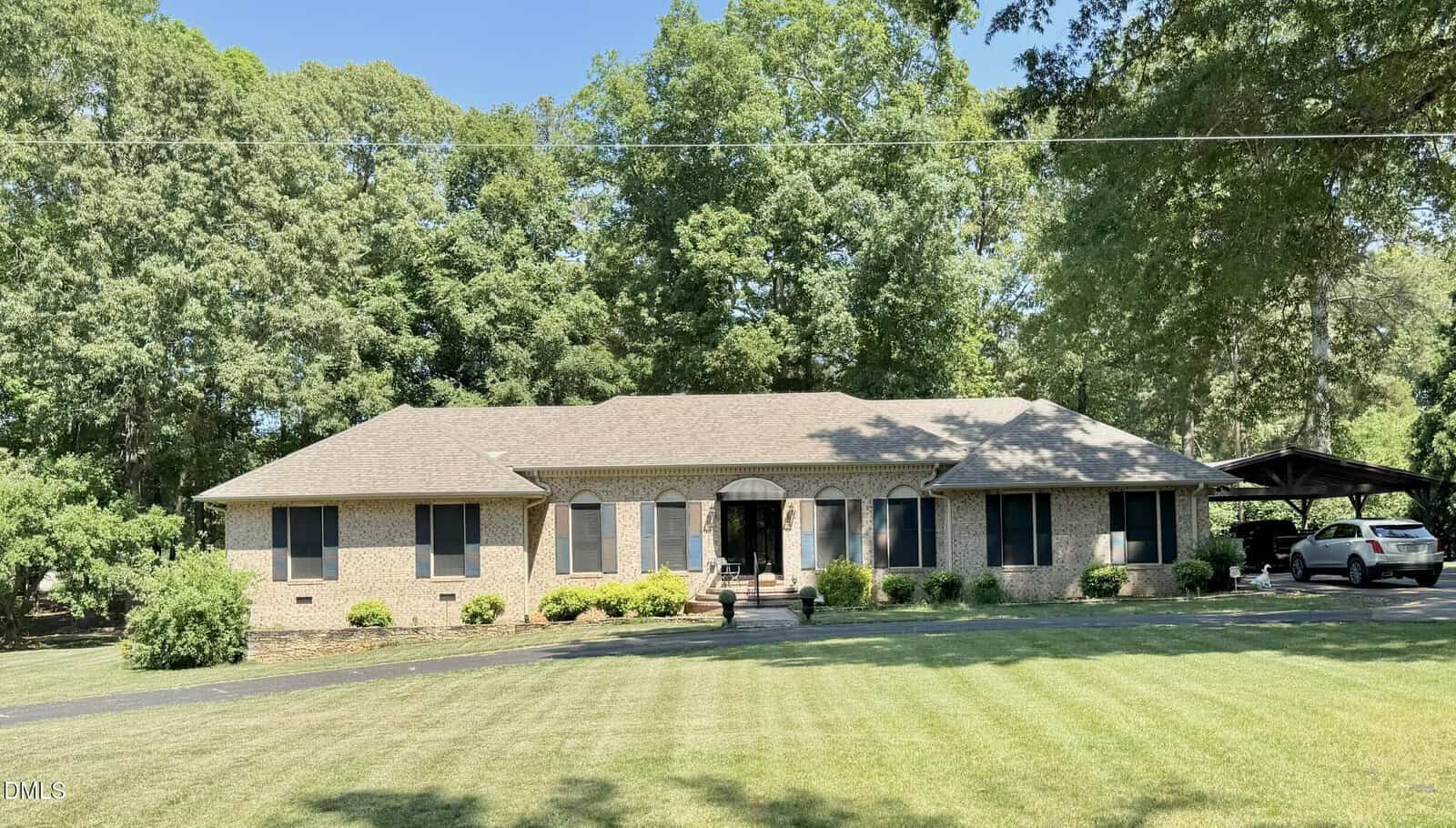 Charming single-story brick house at 1080 Hedrick Drive, Henderson, with dark shutters and a gray roof. Set on a large, neatly mowed lawn with trees behind, the home features a carport and landscaped shrubs along the front.