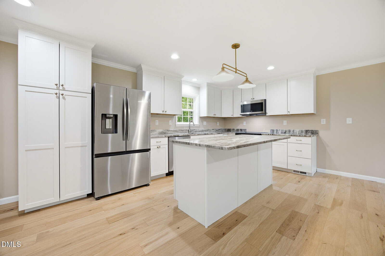 Modern kitchen with white cabinets, stainless steel appliances, marble countertops, center island, light wood flooring, and a gold pendant light fixture. A window above the sink lets in natural light.