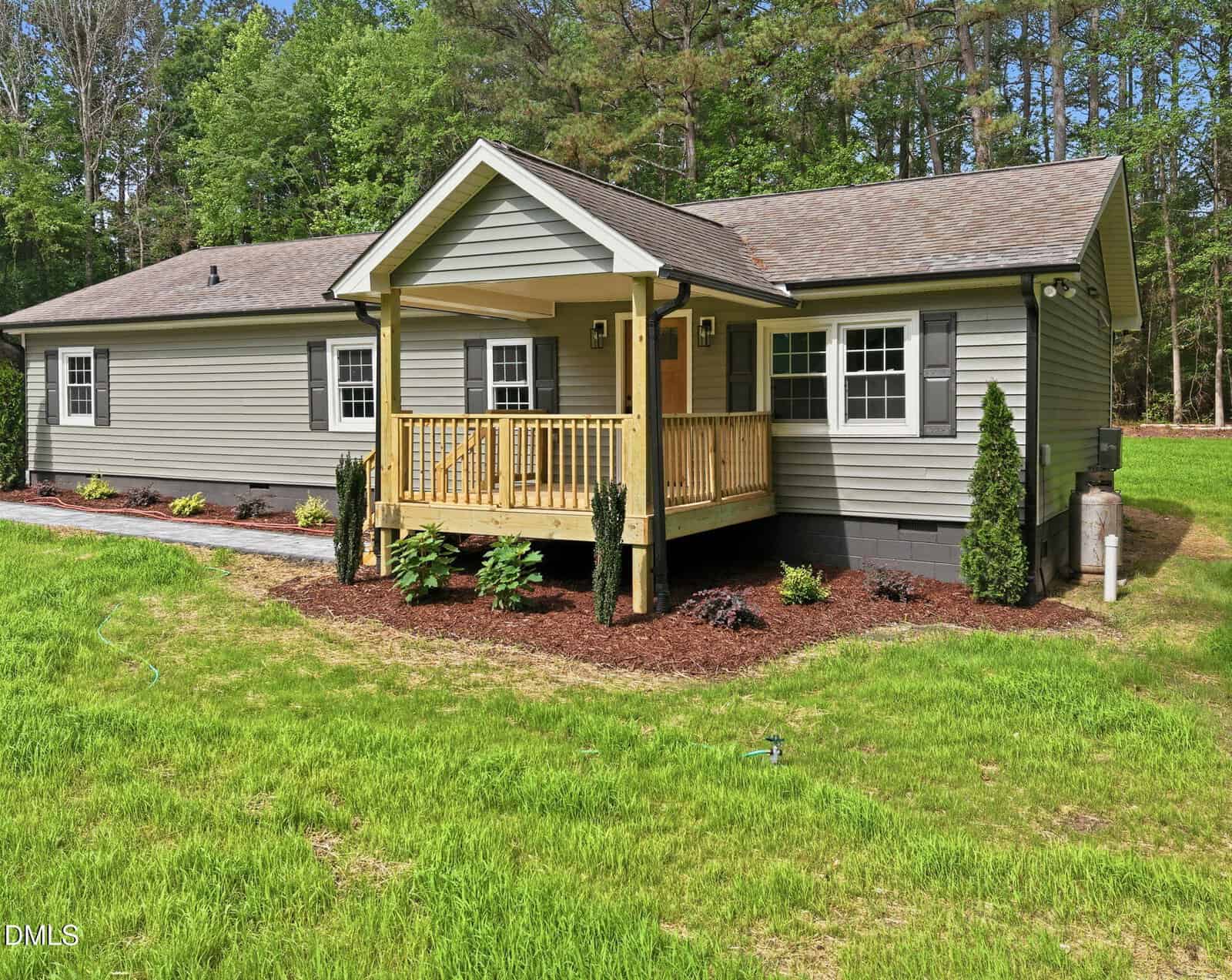 Charming single-story house at 4105 Culbreth Road, Stem, featuring gray siding, a cozy covered front porch with wooden railings, and a gable roof; surrounded by green grass, landscaping, and trees in the background.