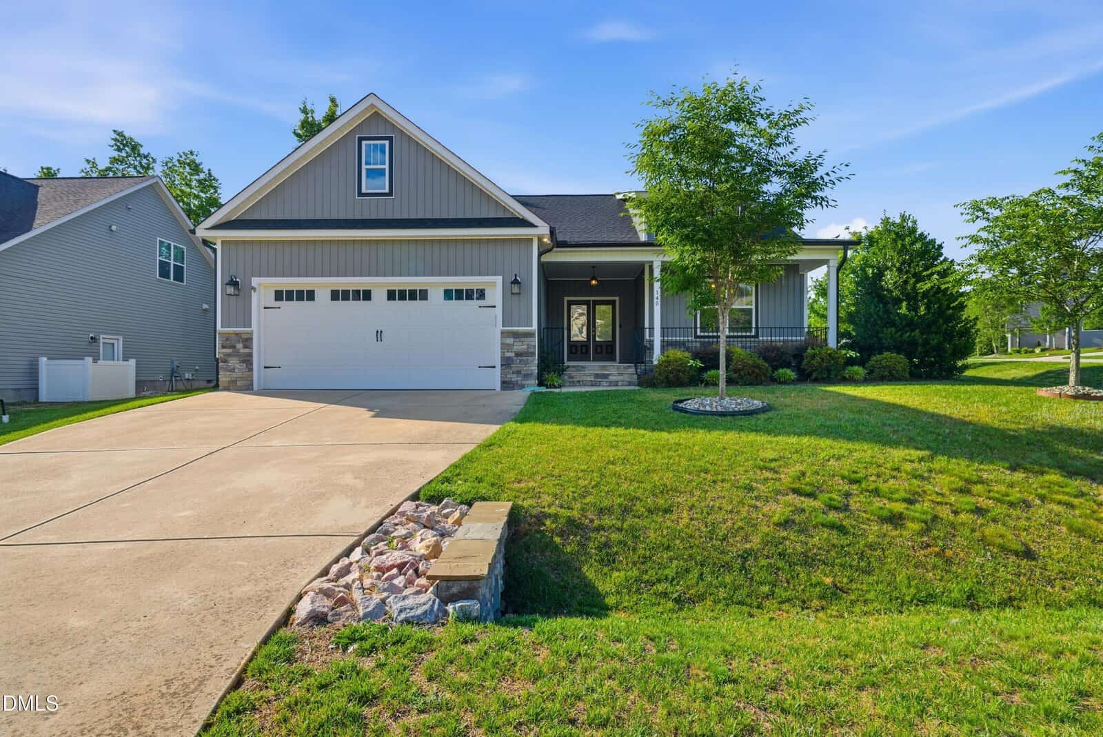 Single-story suburban house in Youngsville with a gray facade, stone accents, double garage, and front porch. The yard at 145 Walking Trail boasts green grass, small trees, and a paved driveway under a clear blue sky.