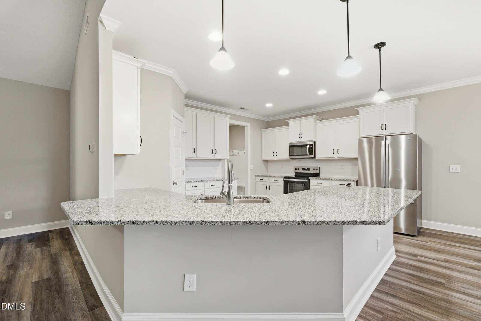 Modern kitchen with white cabinets, stainless steel appliances, granite countertops, and pendant lighting. The room has light walls, wood-style flooring, and an island with a sink and faucet.