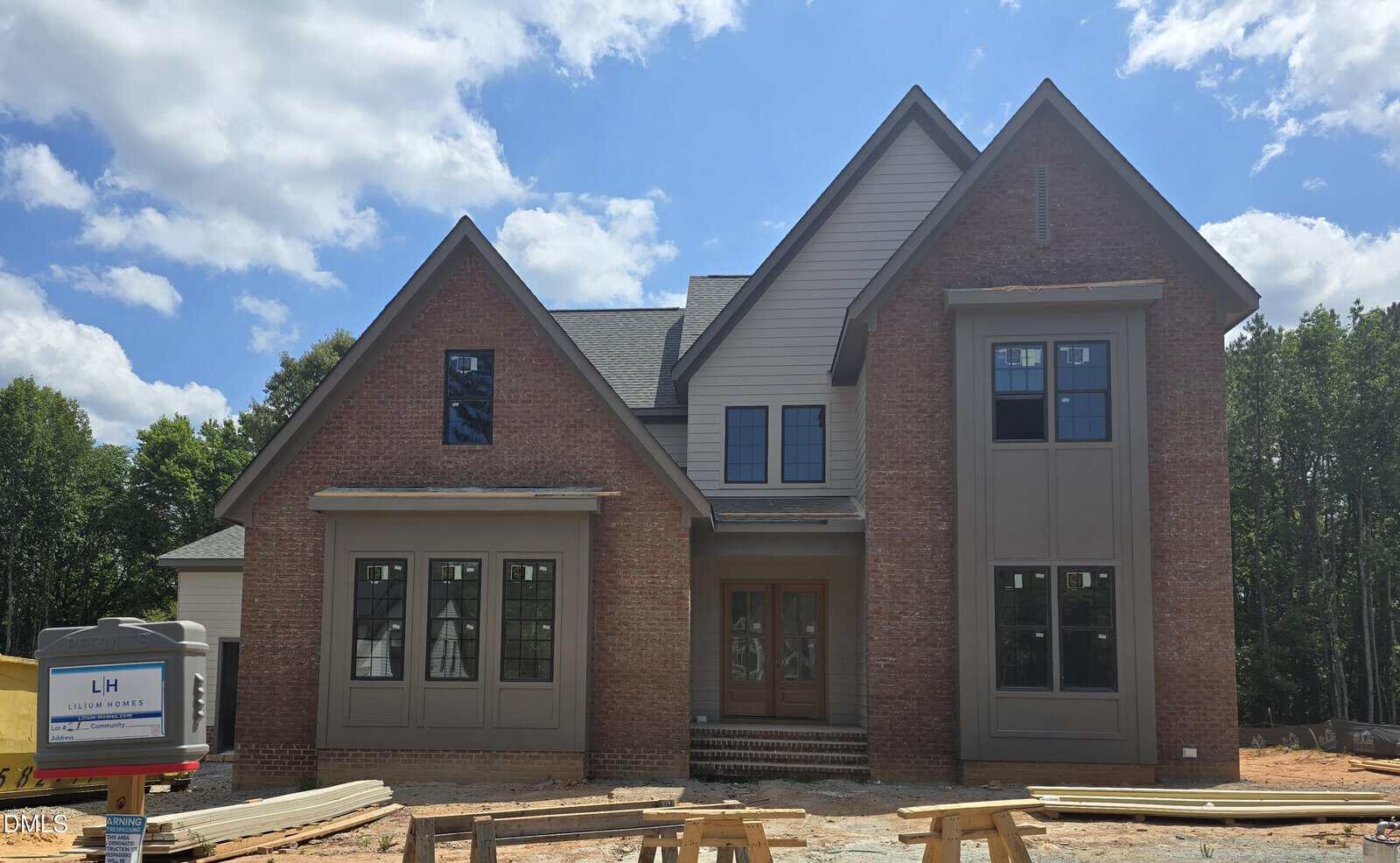 A two-story brick and siding house under construction at 3914 Cedar Knolls Drive in Youngsville, with large front windows, a wooden double front door, unfinished landscaping, and building materials in the foreground. Trees and blue sky complete the scene.