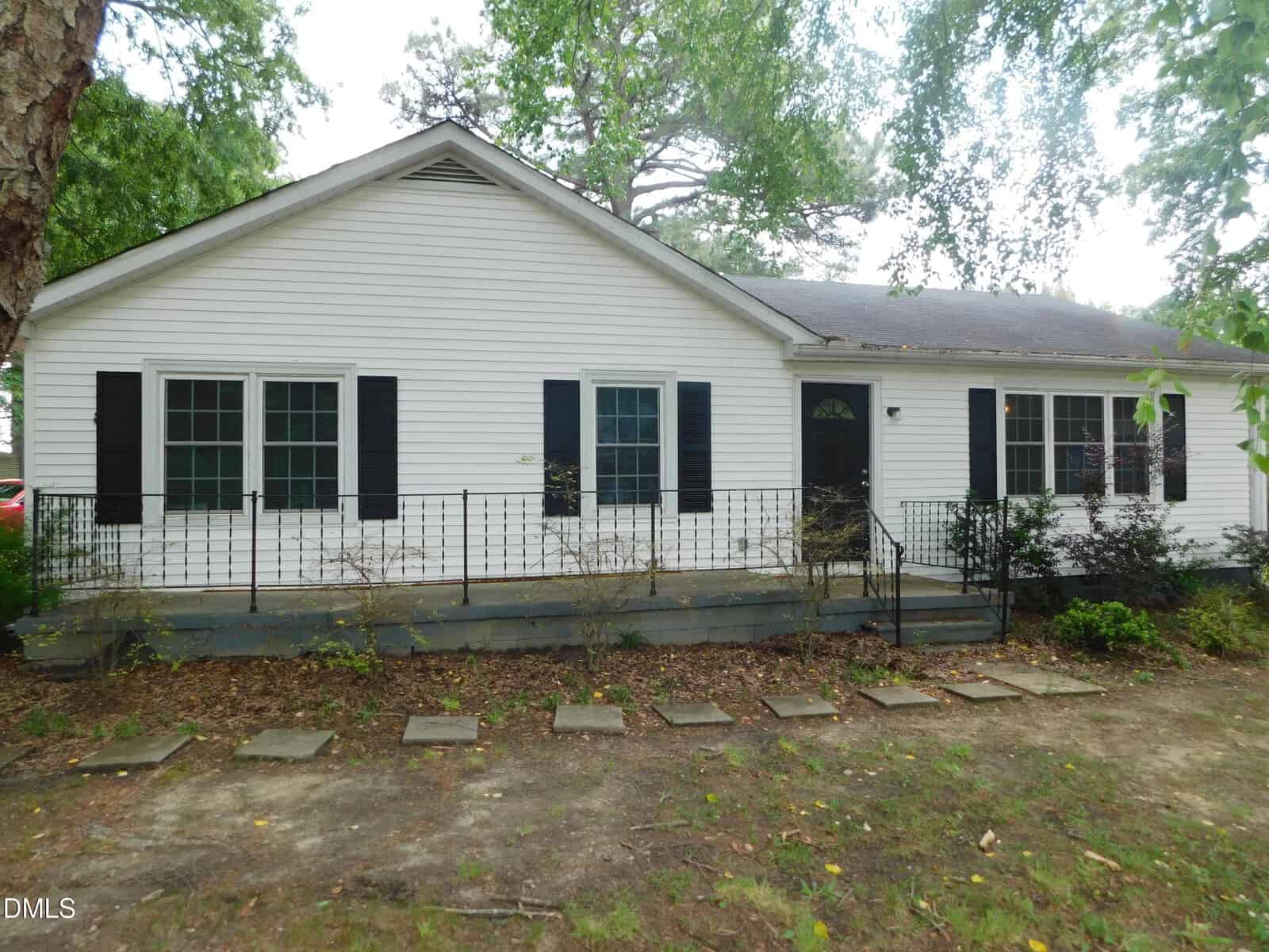 Charming single-story white house at 1536 Hight Street, Henderson, with black shutters, a black front door, and a small porch with metal railing. The front yard features stepping stones and minimal landscaping with trees and shrubs.