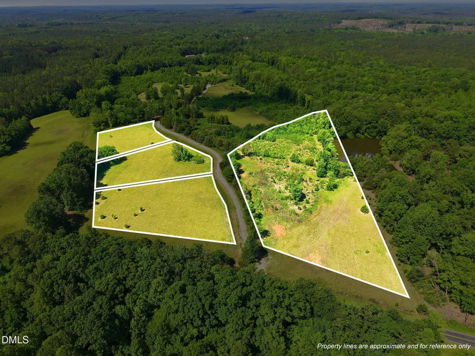 Aerial view of two green, partially wooded land parcels outlined in white, separated by a road, surrounded by dense forest and open fields under a clear sky.