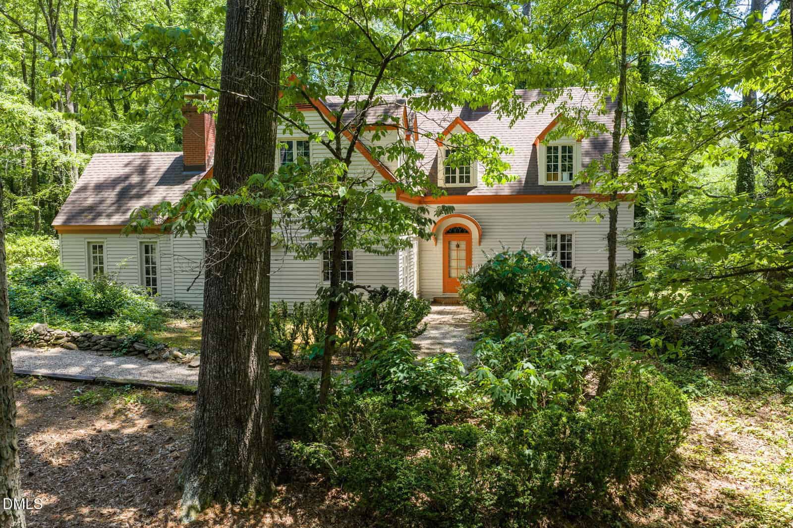 A white two-story house with orange trim and a prominent arched front door sits at 418 Fairview Street in Warrenton, surrounded by lush green trees and dense foliage in a forested setting.