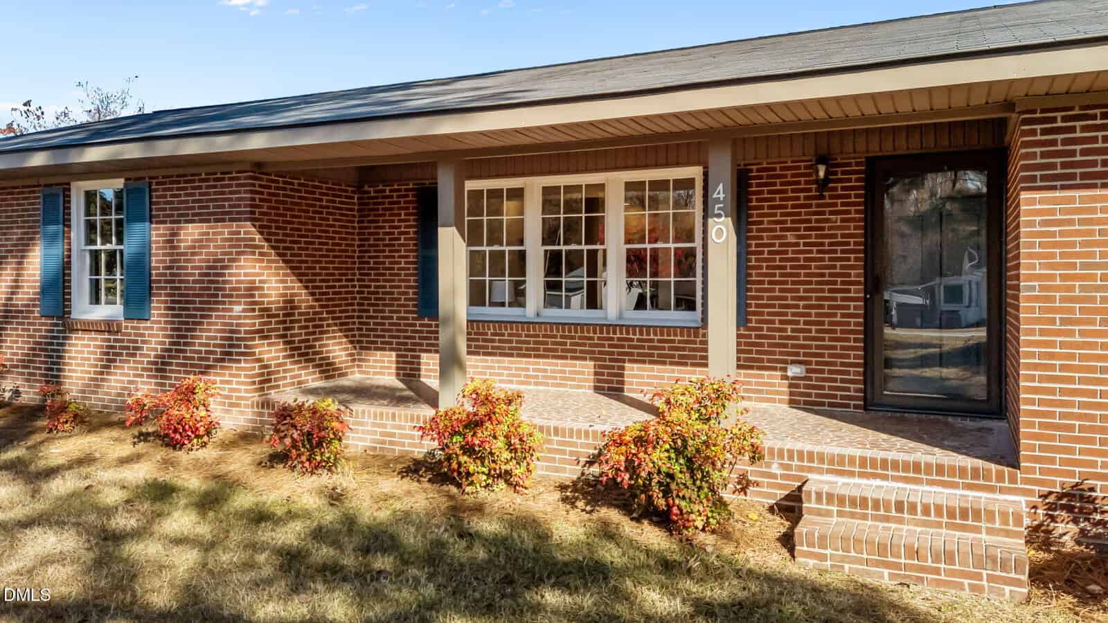 A single-story red brick house with white-trimmed windows, a covered front porch, gray columns, steps, and small shrubs along the front walkway. The house number 450 is displayed beside the front door.