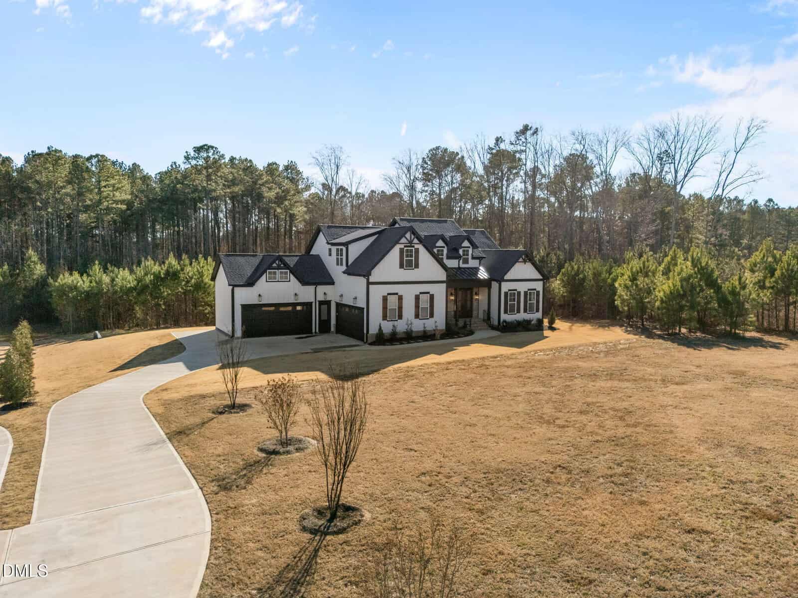 A large two-story house with a white exterior and black roof sits on a spacious, dry grassy lot at 3214 Bruce Garner Road in Creedmoor, surrounded by trees, with a curved driveway leading to a three-car garage.