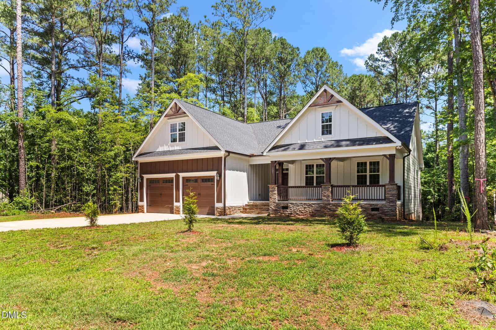 A modern farmhouse-style home at 121 Quarterhorse Drive in Louisburg, featuring white siding, stone accents, a covered front porch, and a two-car garage, surrounded by trees and greenery on a sunny day.