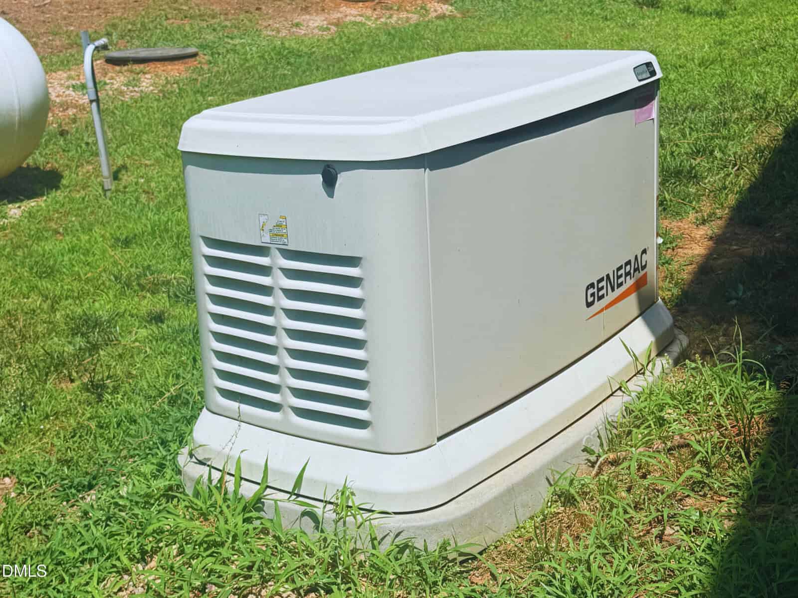 A white Generac backup generator sits on a concrete slab surrounded by green grass, with part of a propane tank visible in the background.