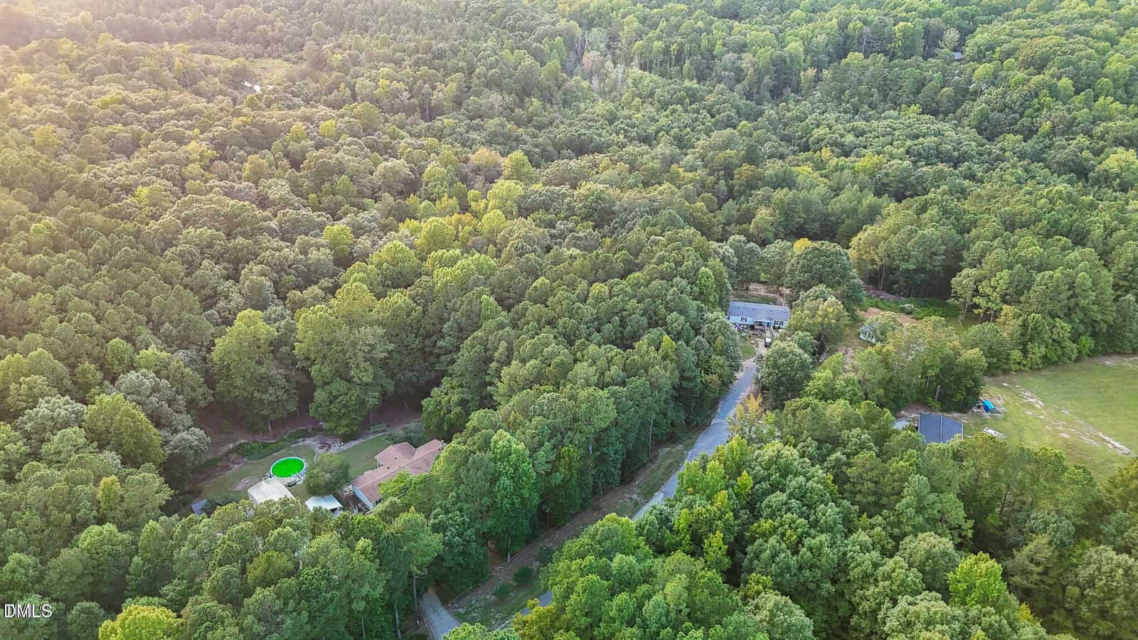 Aerial view of houses in Louisburg, surrounded by dense, green forest, with a winding road and two round pools in backyards near 87 Beaver Court, taken on a sunny day.