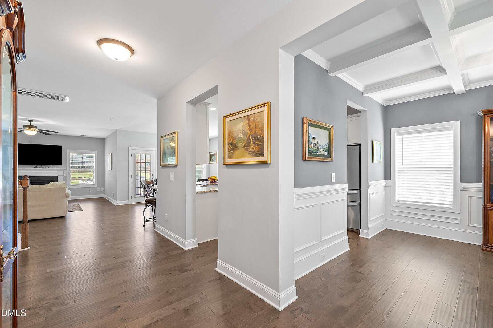 Spacious, modern home interior with hardwood floors, gray and white walls, crown molding, and wall art. Open living room, kitchen, and dining area with natural light from large windows.