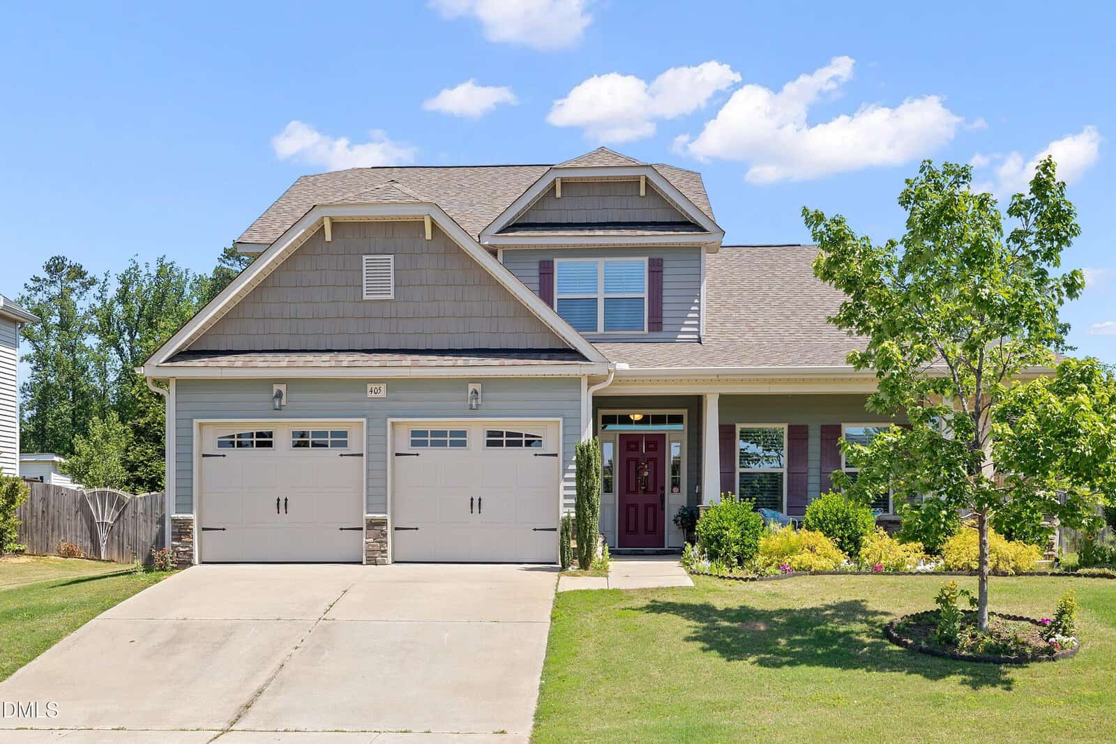 Two-story suburban house in Youngsville with a gray exterior, double garage, red front door, and small covered porch. Located on 405 Club Center Drive, it features a green lawn, a tree, and landscaped bushes under a sunny blue sky.
