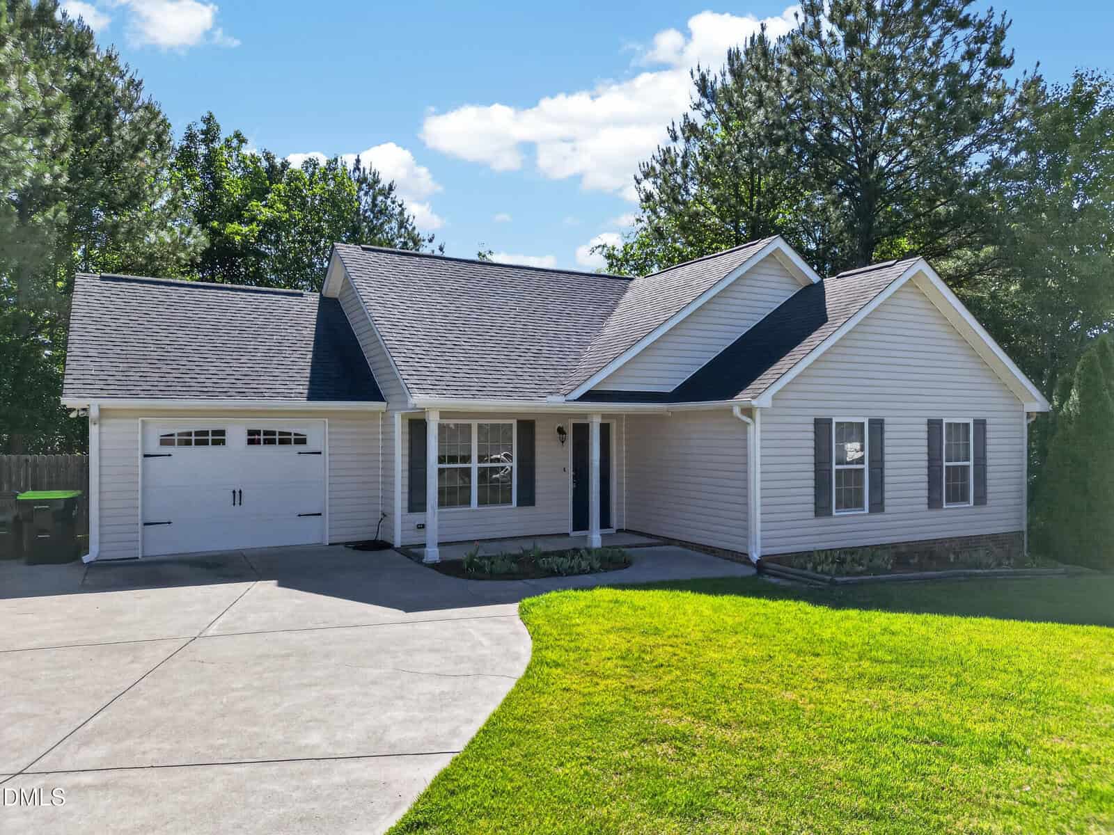 Charming single-story house at 103 Dundee Place with light-colored siding, a gabled roof, attached garage, and concrete driveway. Black shutters accent the windows, while green grass and trees stem from the landscaped front yard.
